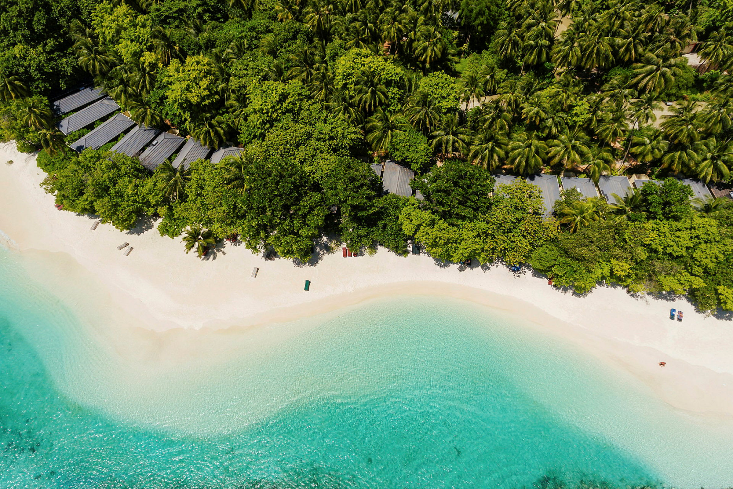 Luftfoto der viser en tropisk strand med hvidt sand, omgivet af klart blåt vand og frodig vegetation. (AI-genereret tekst)