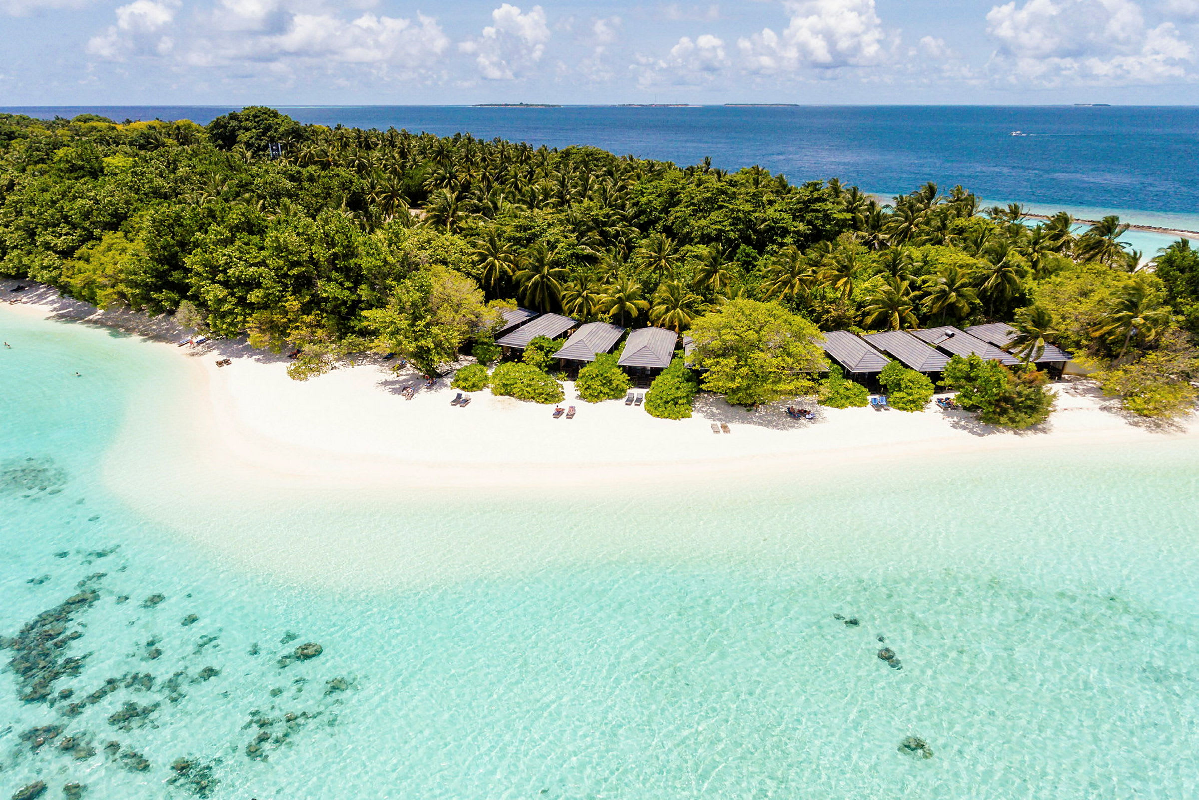 En tropisk strand med klart turkis vand, bungalower og tæt vegetation. (AI-genereret tekst)