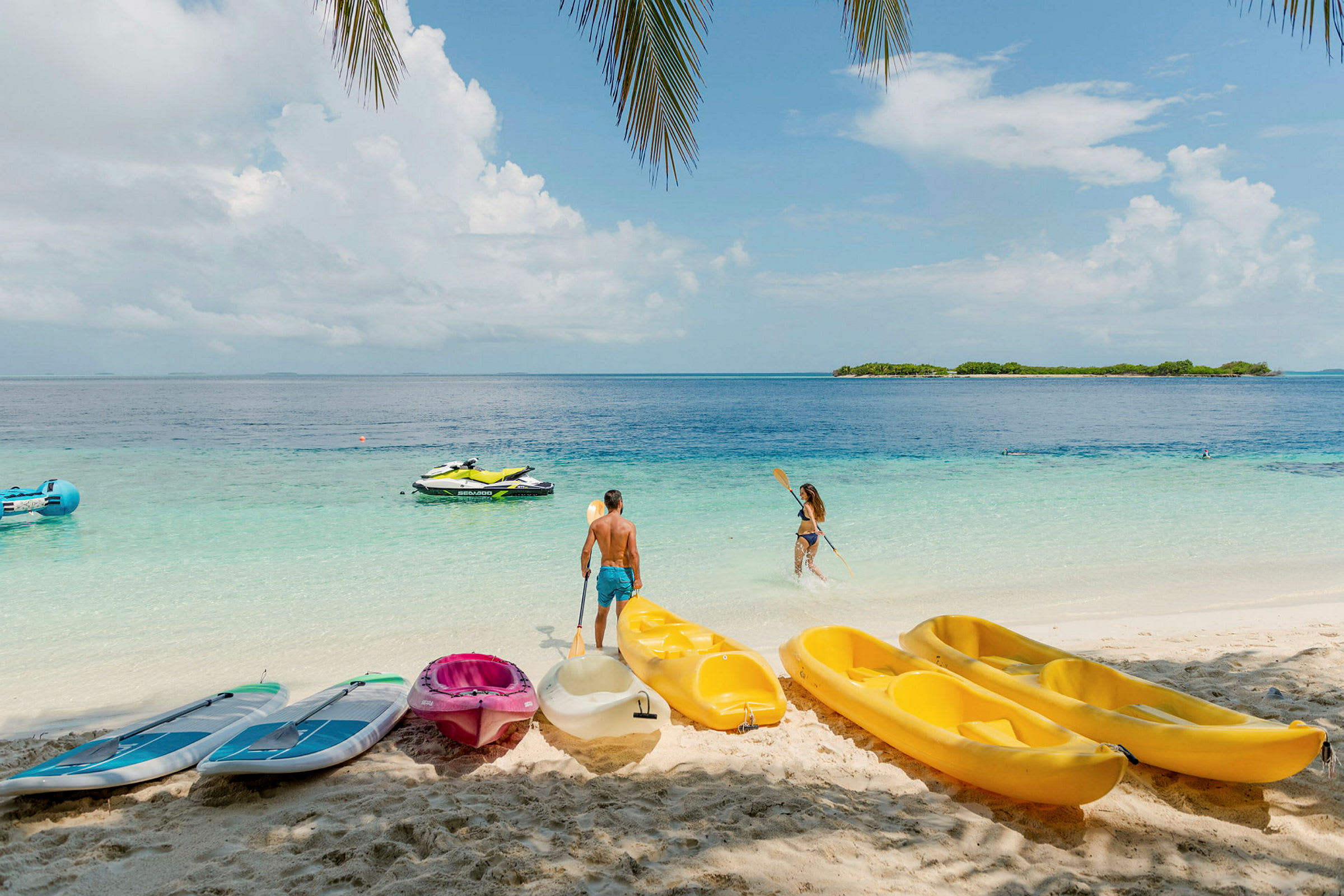Personer på stranden med kajakker og paddleboards samt vandscooter på havet. (AI-genereret tekst)