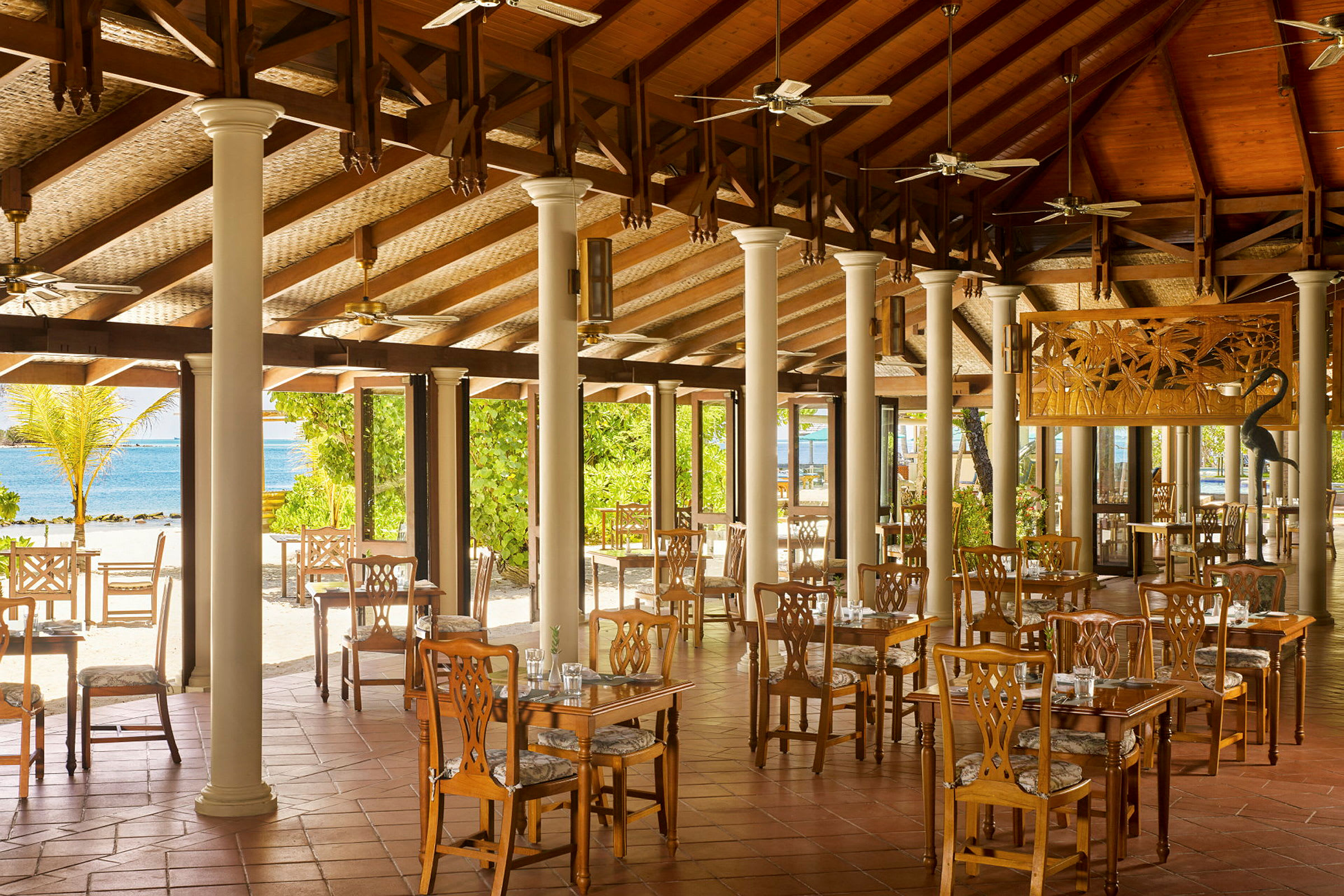 Restaurant med træborde og stole, åbne områder og udsigt til stranden og havet. (AI-genereret tekst)