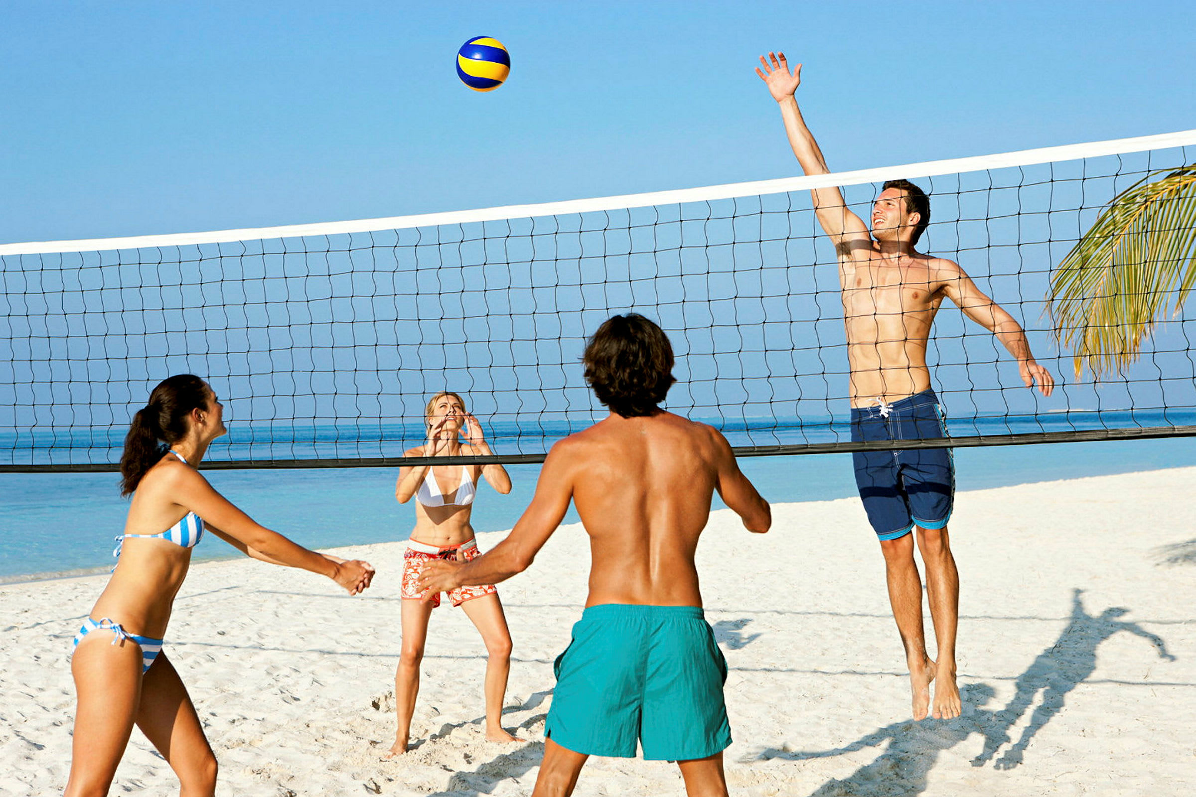 Fire personer spiller strandvolleyball på en sandstrand ved havet. (AI-genereret tekst)