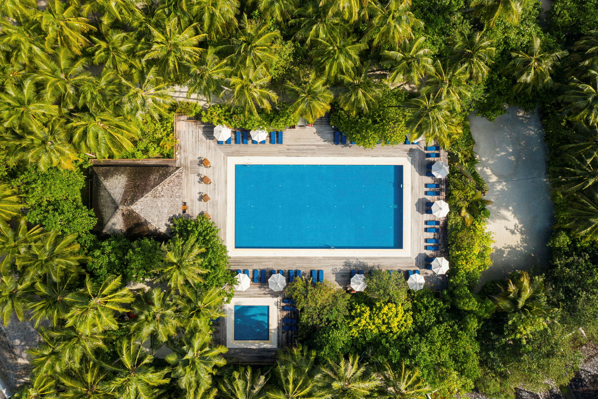 Luftfoto af en udendørs pool omgivet af vegetation og liggestole. (AI-genereret tekst)