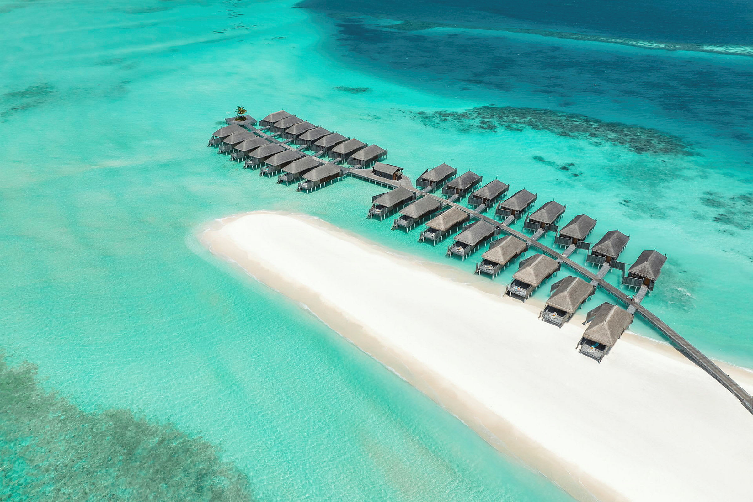 Bungalows på pæle over klart turkis vand ved en hvid sandstrand. (AI-genereret tekst)