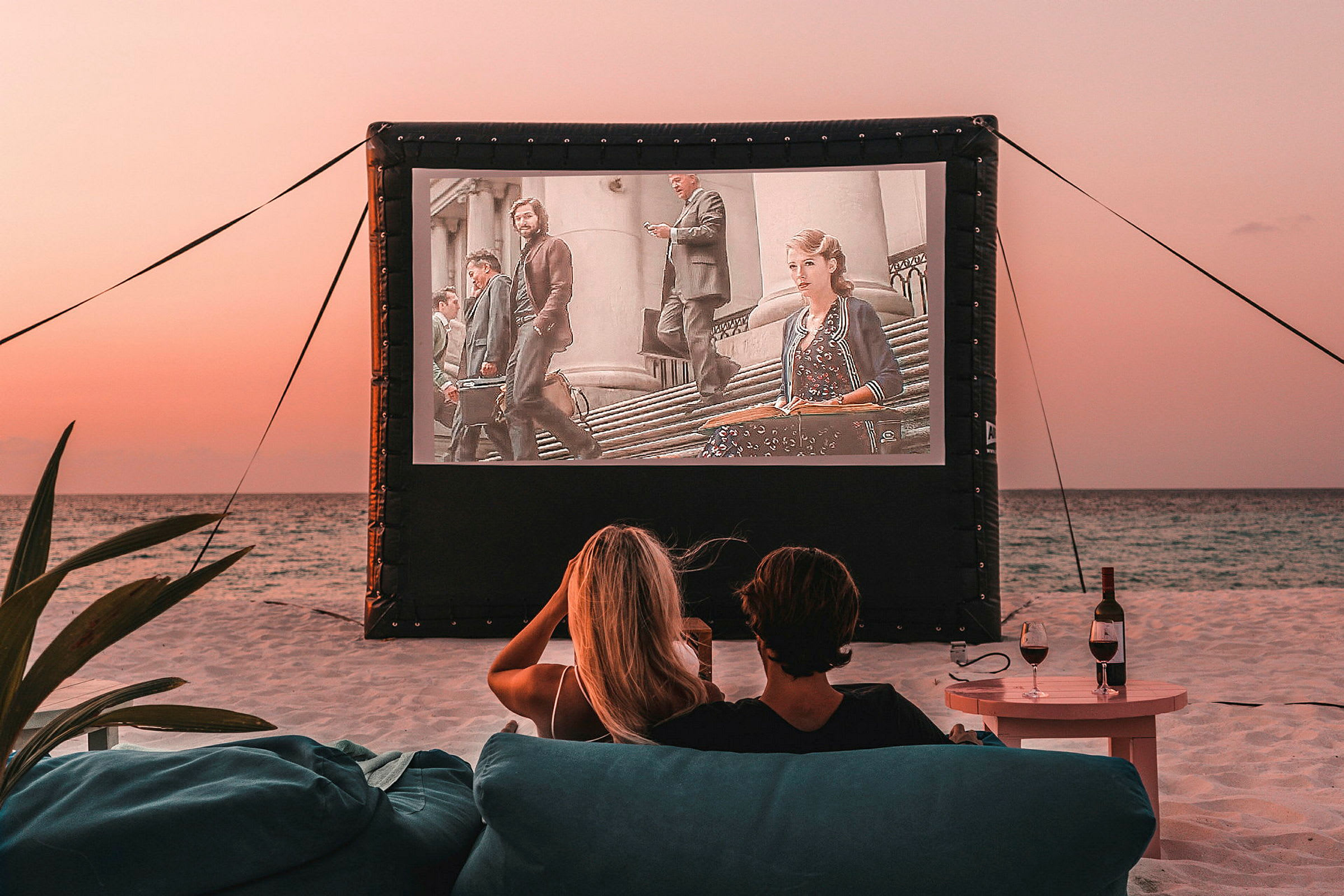 To personer sidder på stranden og ser en film, der vises på et udendørs lærred. (AI-genereret tekst)