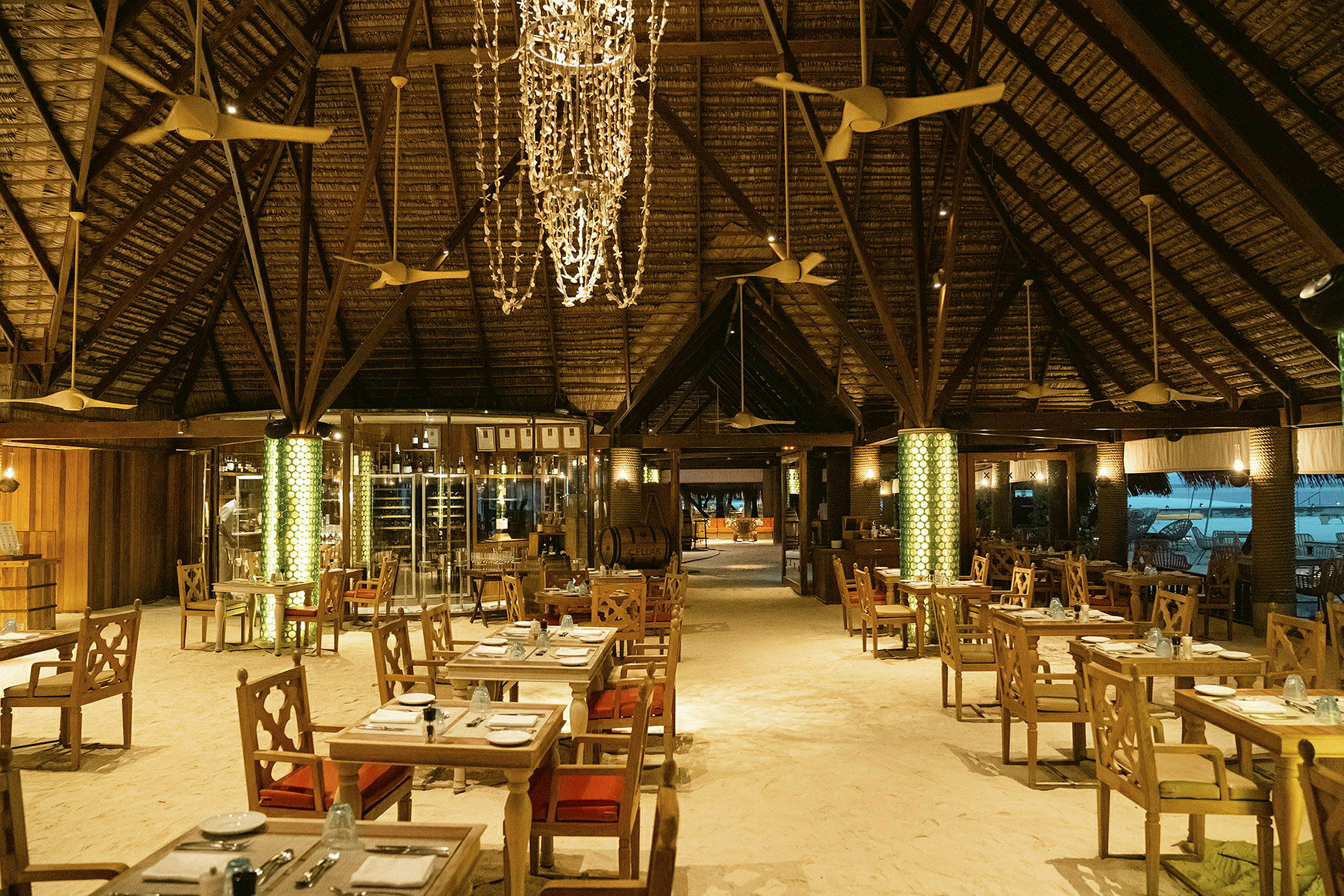 Restaurant med borde på sandgulv og en dekorativ loftlampe. (AI-genereret tekst)