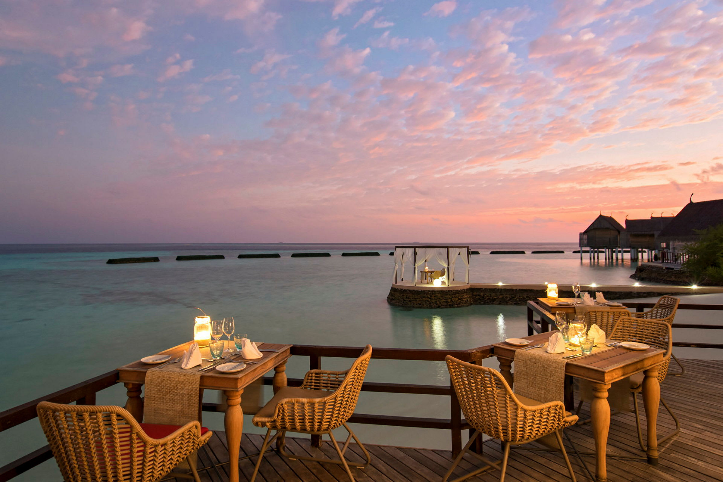 Udendørs servering på en terrasse med udsigt over havet ved solnedgang. (AI-genereret tekst)