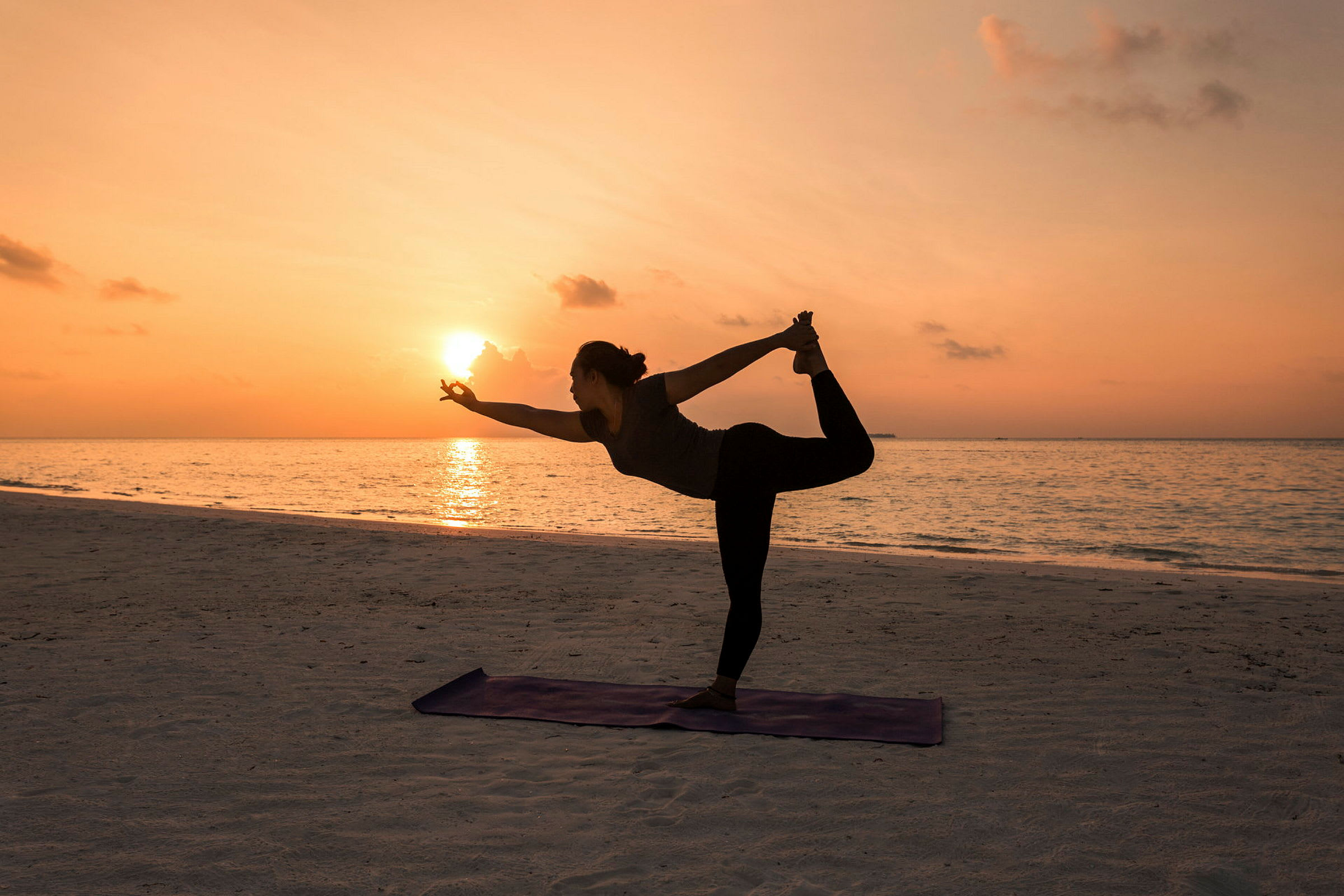 Silhuetten af en person, der udfører yoga på stranden ved solnedgang. (AI-genereret tekst)
