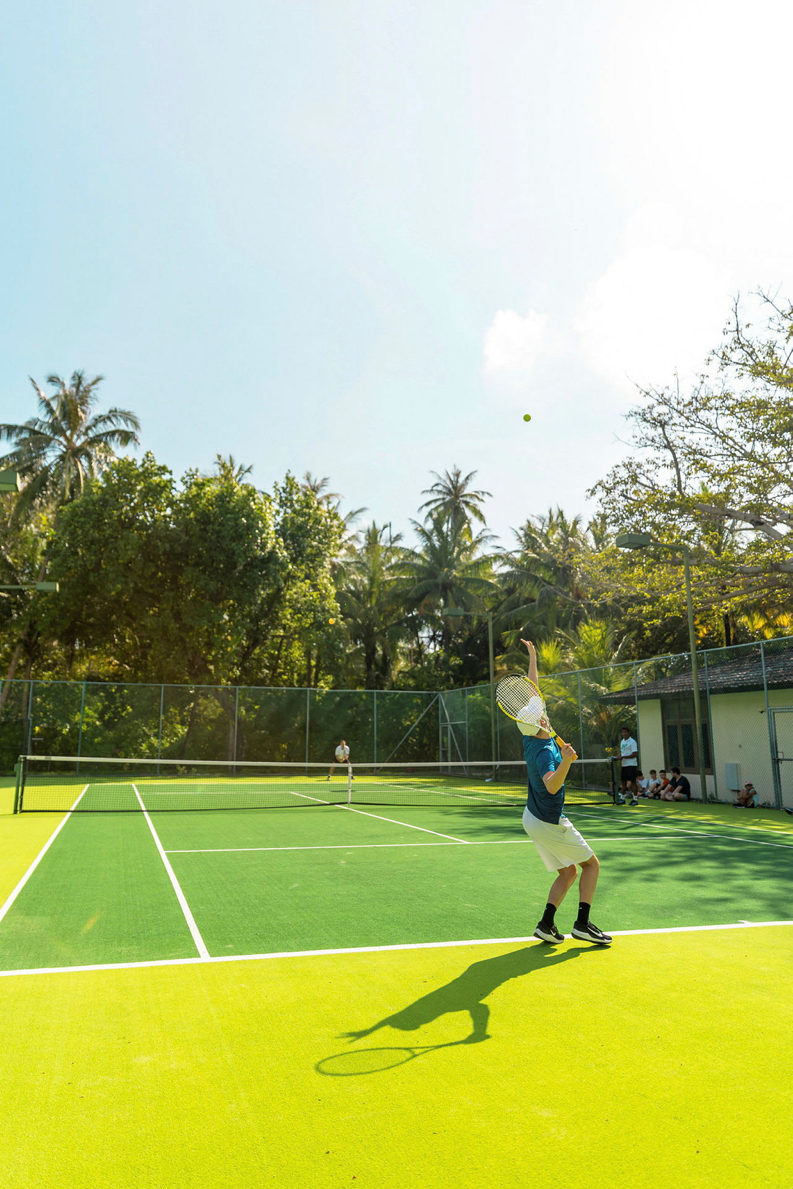 En person spiller tennis på en udendørsbane omgivet af træer. (AI-genereret tekst)