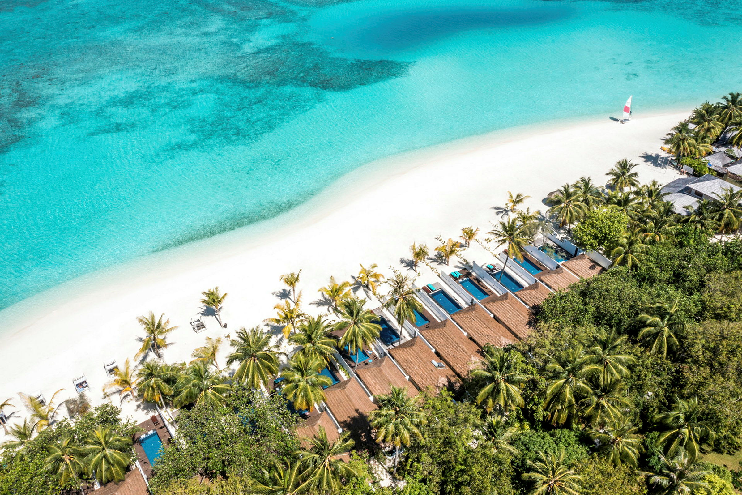 Luftfoto af en tropisk strand med hvidt sand, turkis hav, palmer og private bungalower med pools. (AI-genereret tekst)