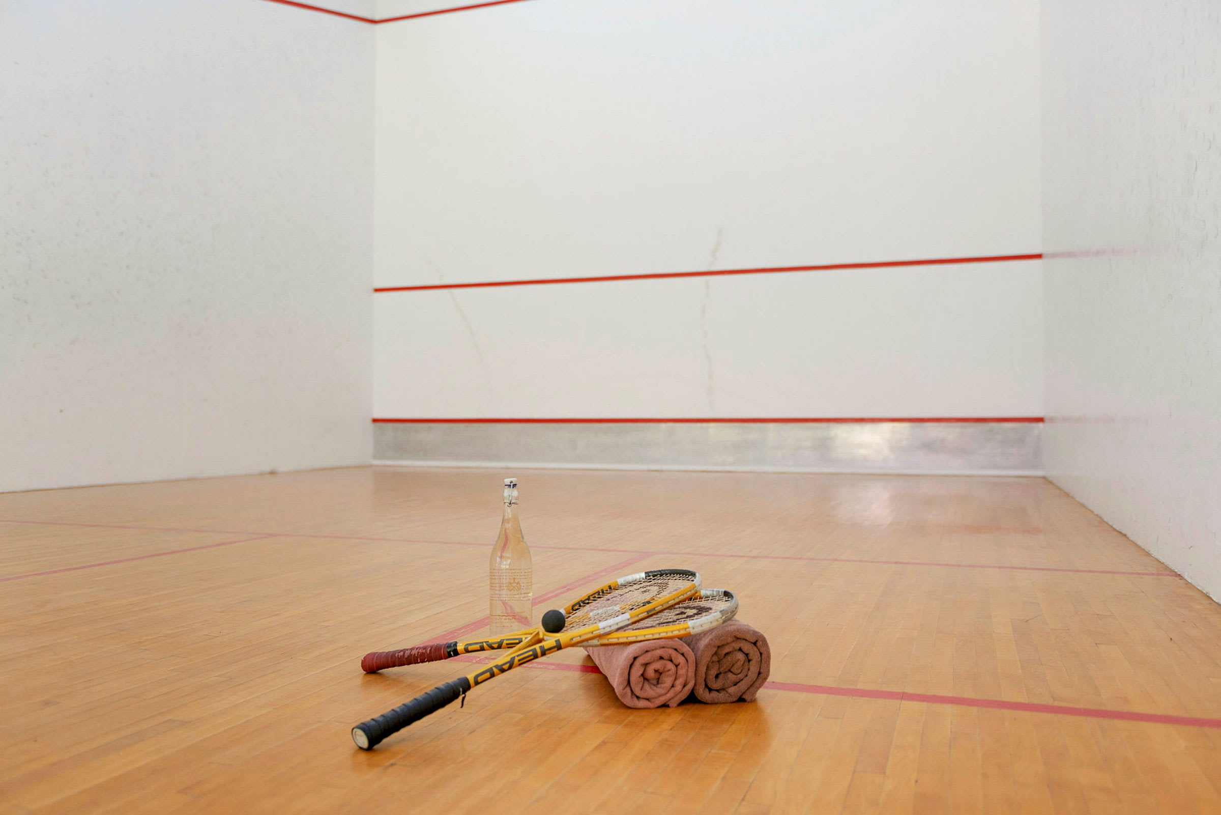 Squashketchere, håndklæder og en vandflaske ligger på gulvet på en squashbane. (AI-genereret tekst)