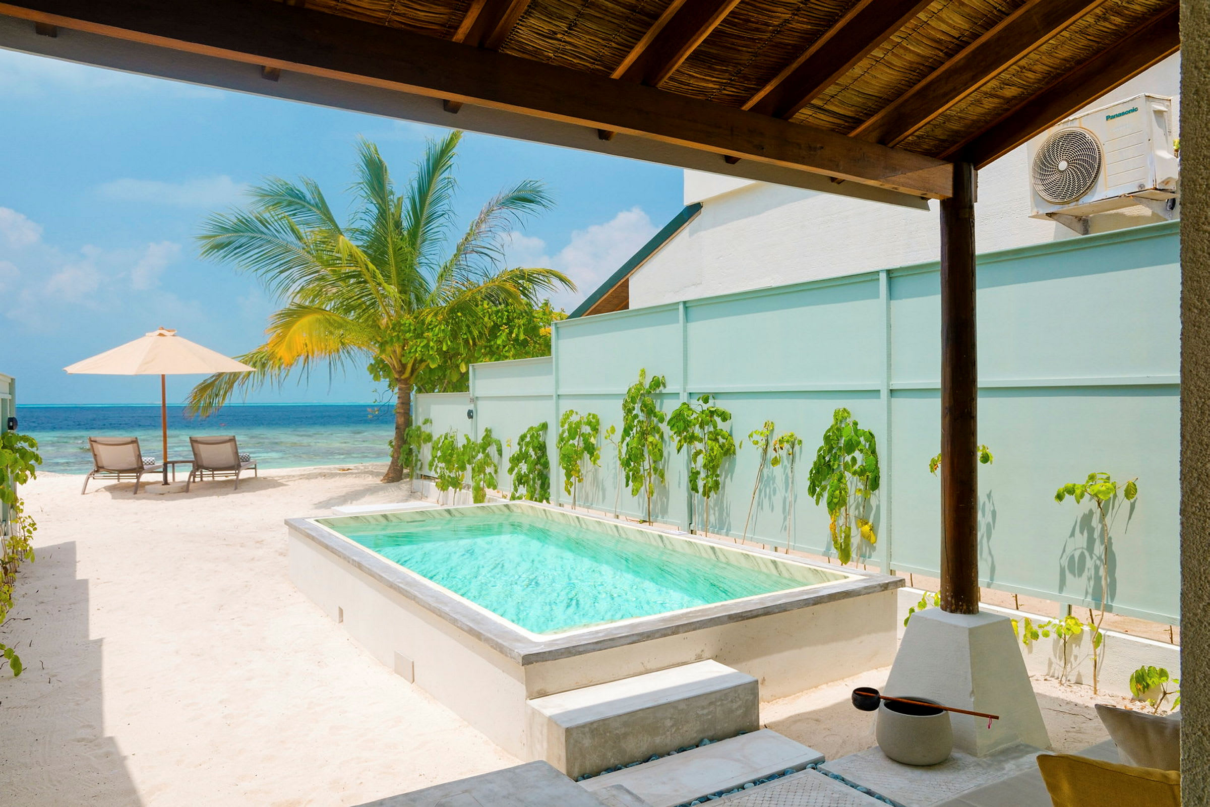 Privat pool med udsigt til havet, omgivet af sand og palmetræ under skyggende tag. (AI-genereret tekst)