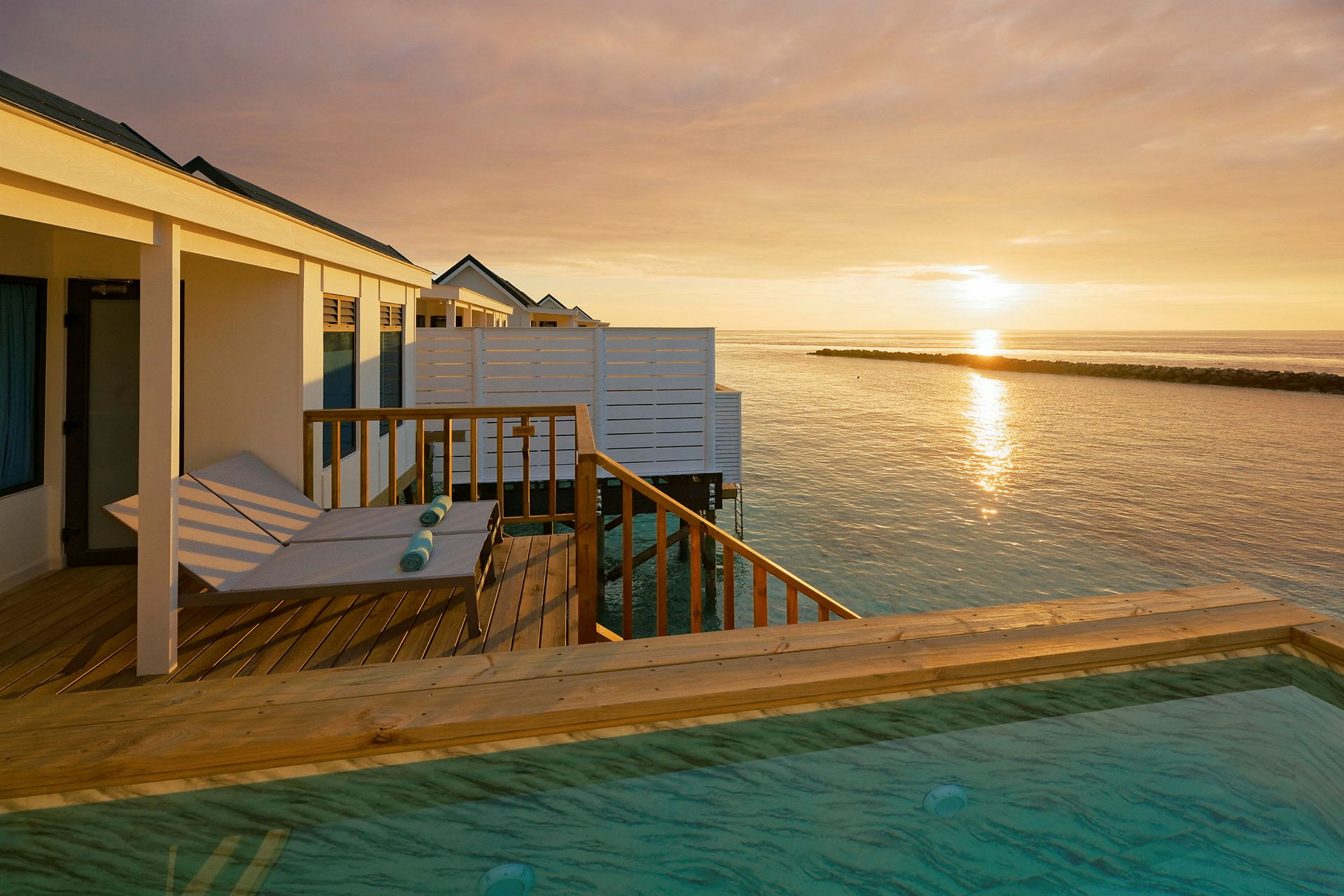 Solnedgang over havet med overnatningssteder på vandet og en privat pool. (AI-genereret tekst)