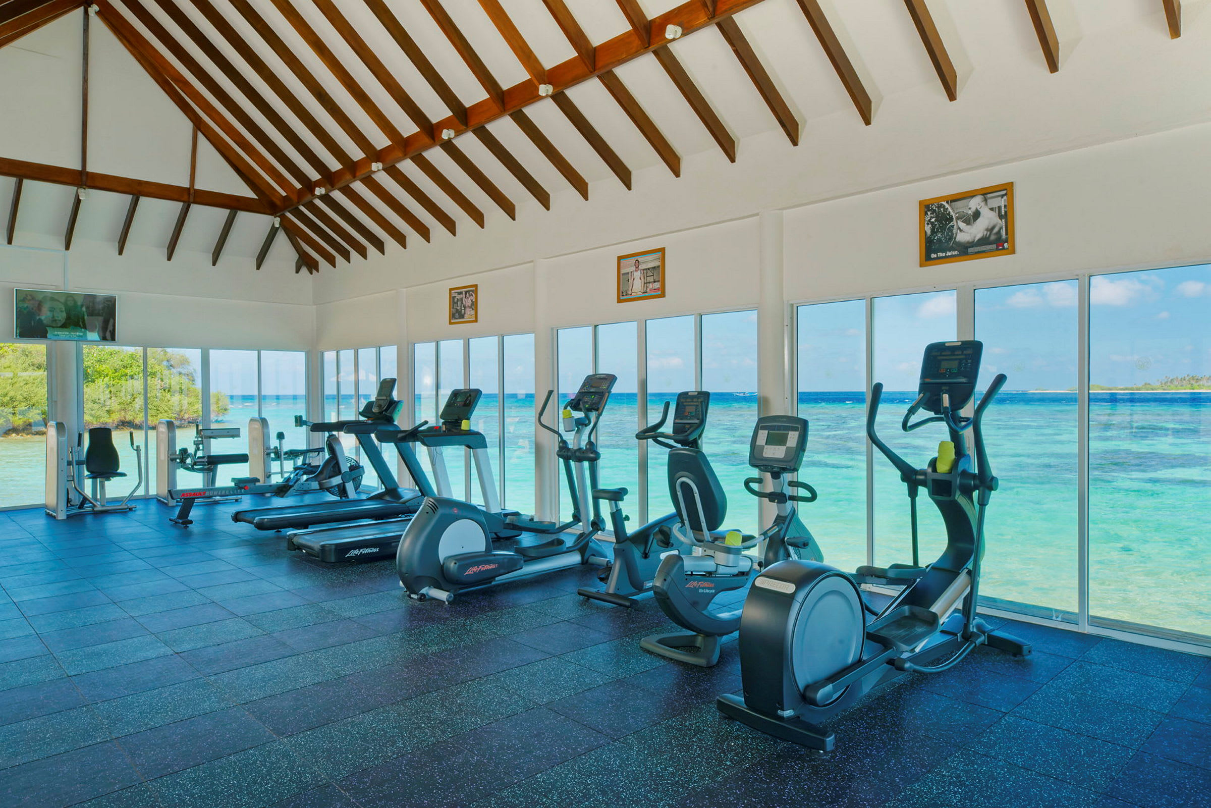 Fitnesscenter med træningsmaskiner og udsigt over havet gennem store glasvinduer. (AI-genereret tekst)