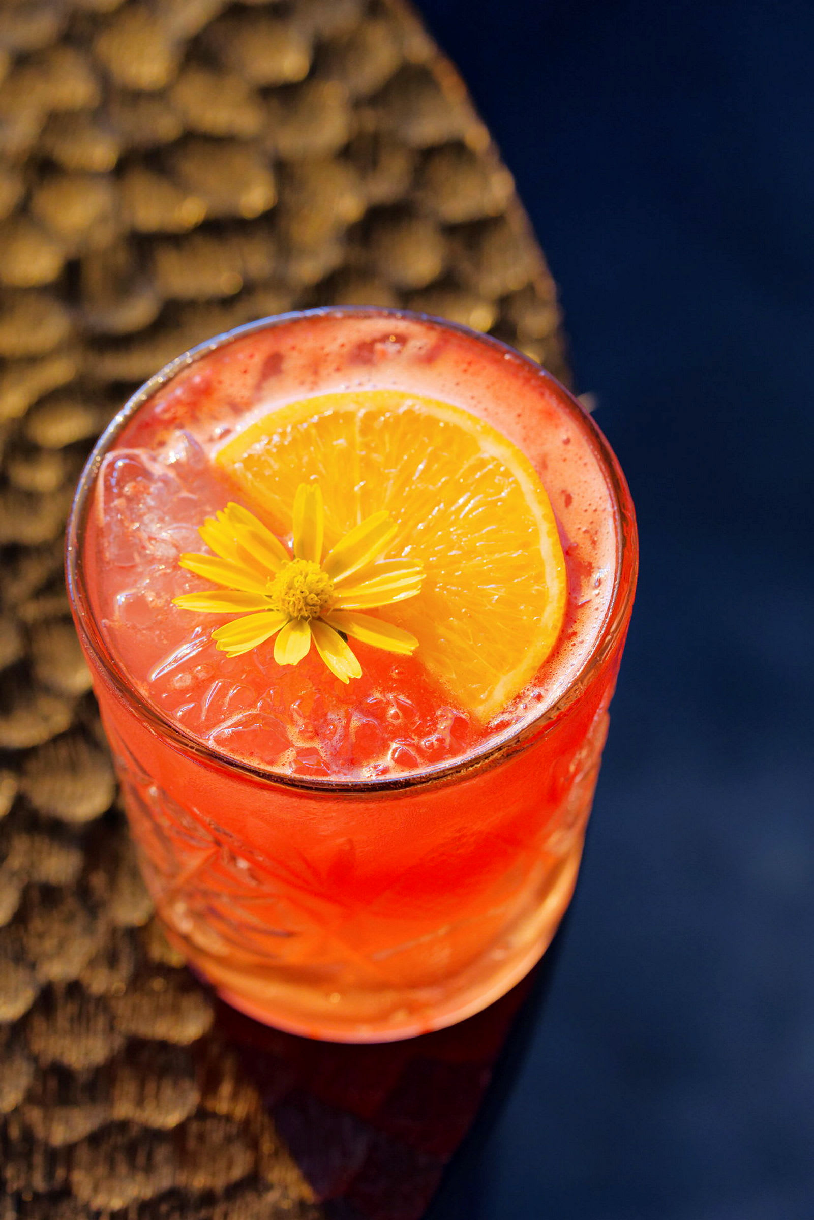 En orange drink serveret i et glas pyntet med en citrus skive og en blomst. (AI-genereret tekst)