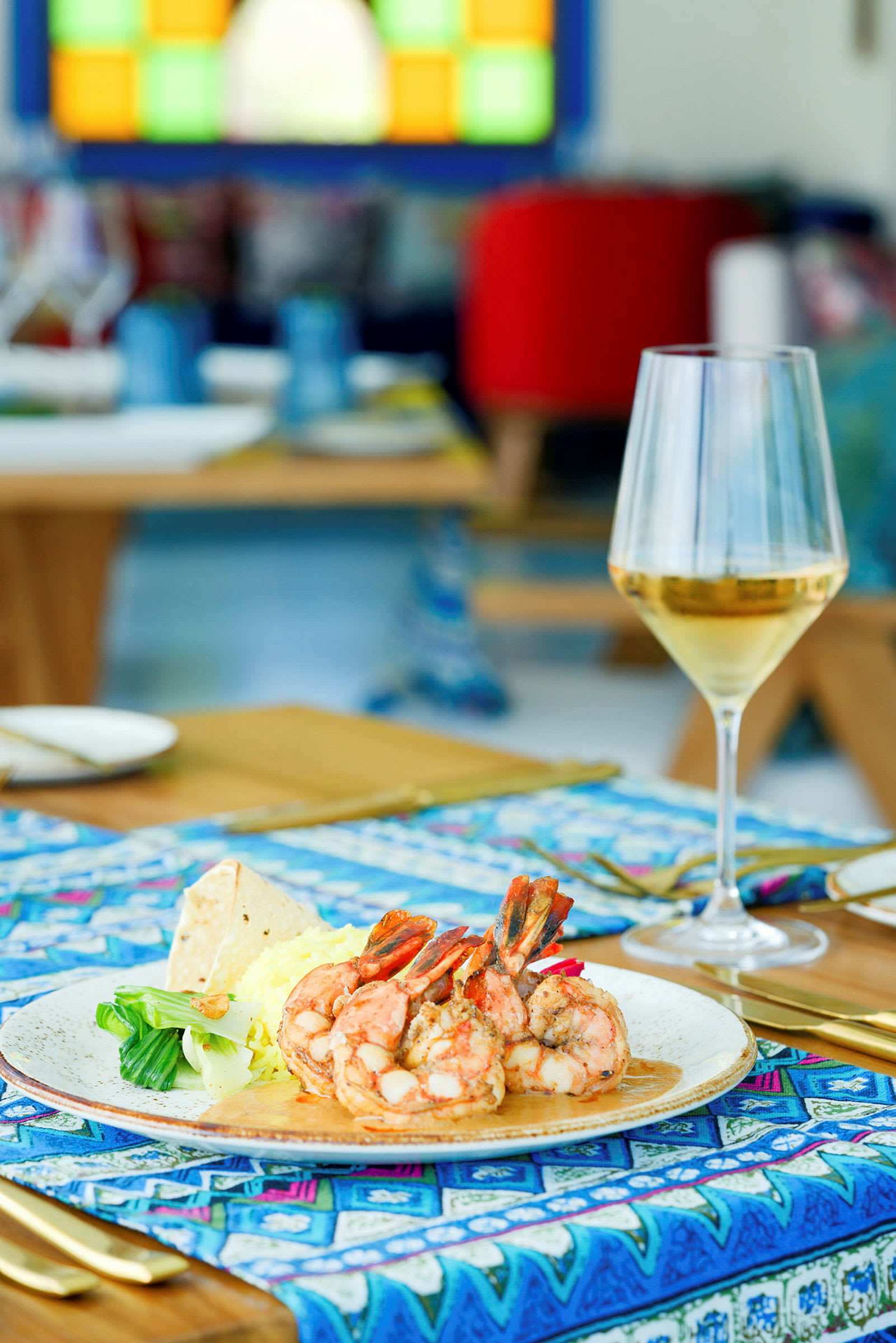 En tallerken med rejer, grøntsager og ris samt et glas vin på et dækket bord. (AI-genereret tekst)