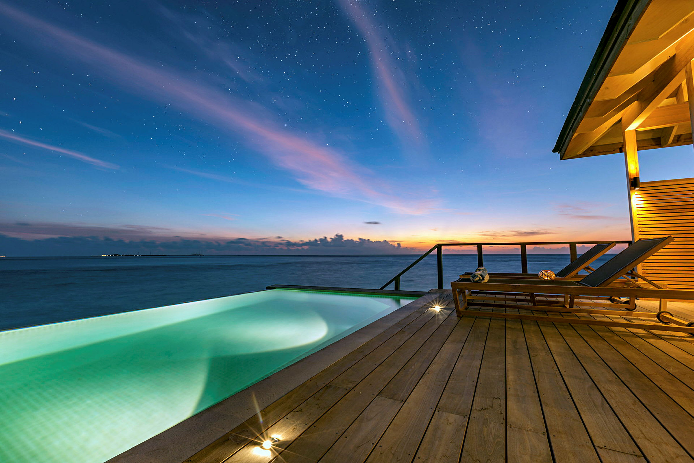 Billedet viser en infinitypool på en terrasse med udsigt over havet under en stjerneklar aften. (AI-genereret tekst)