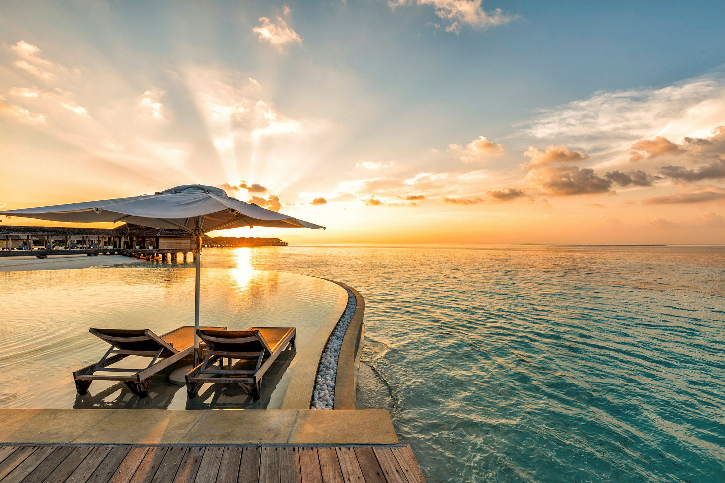 To liggestole med parasol ved en infinity-pool og havet i solnedgang. (AI-genereret tekst)