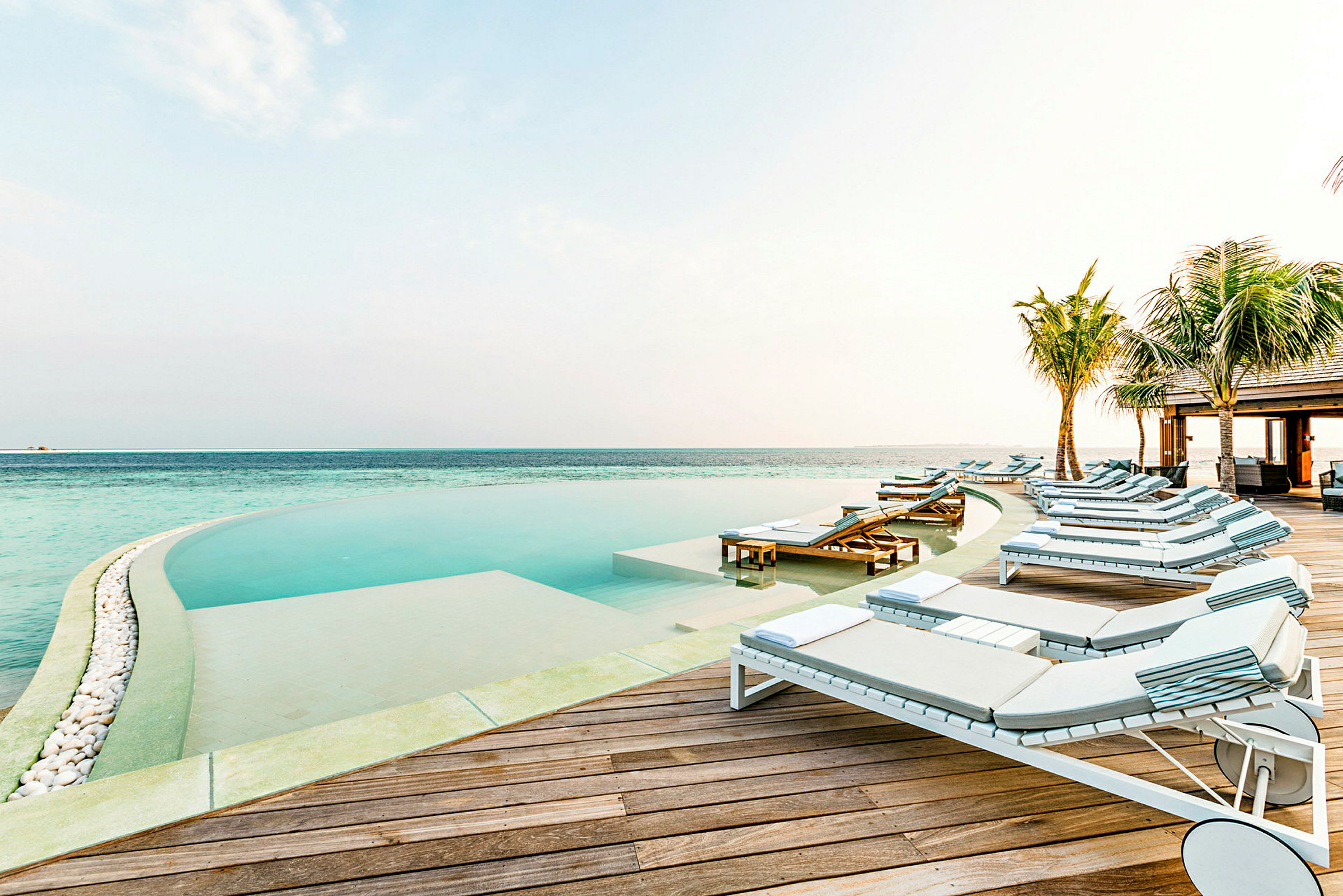 Liggestole ved en infinity-pool tæt på havet. (AI-genereret tekst)