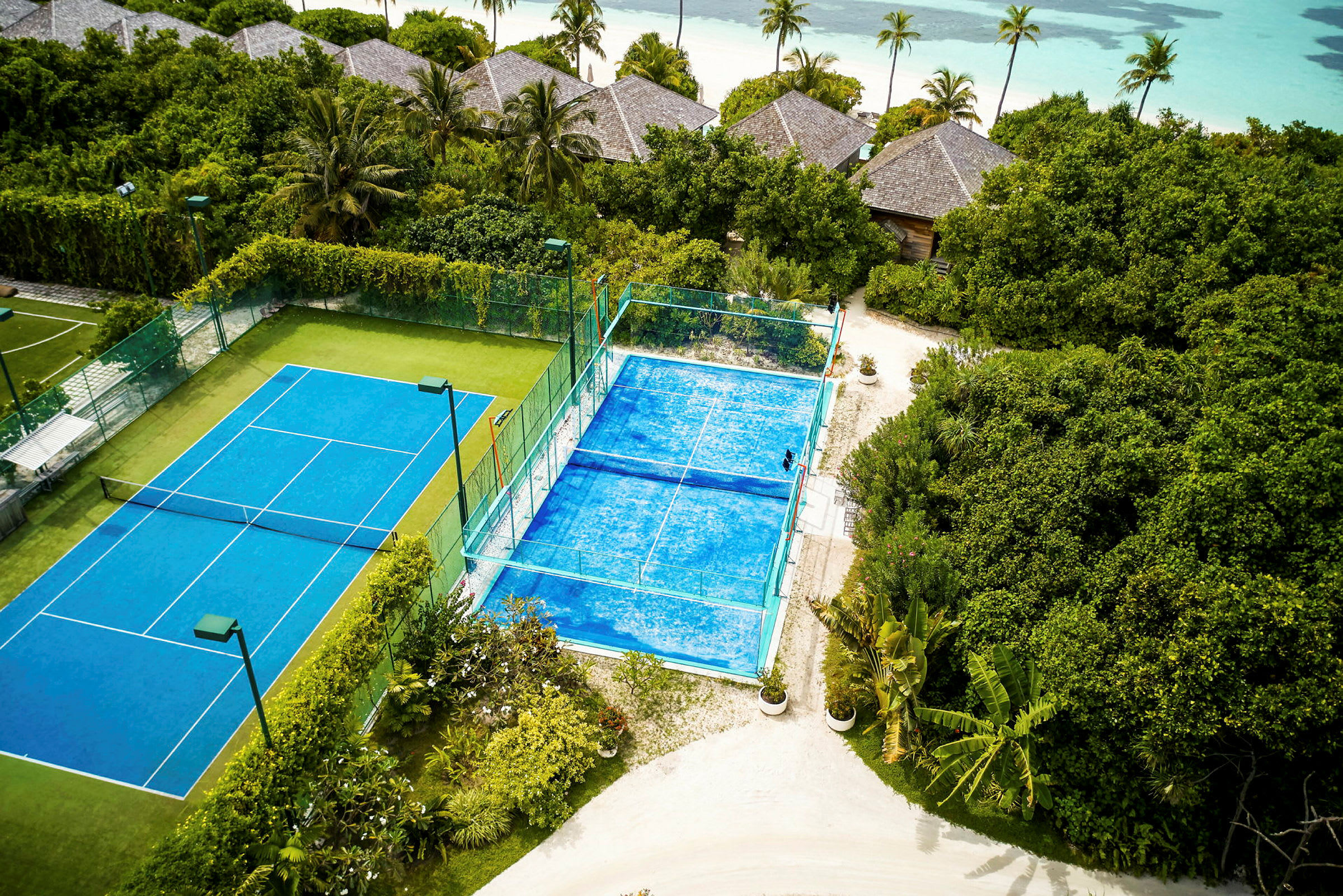 To tennisbaner blandt grønne omgivelser tæt på stranden. (AI-genereret tekst)