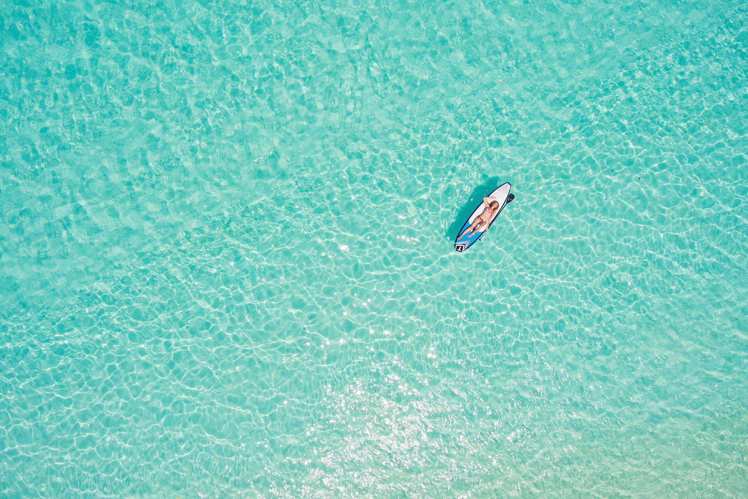 En person ligger på et paddleboard på klart turkis vand. (AI-genereret tekst)
