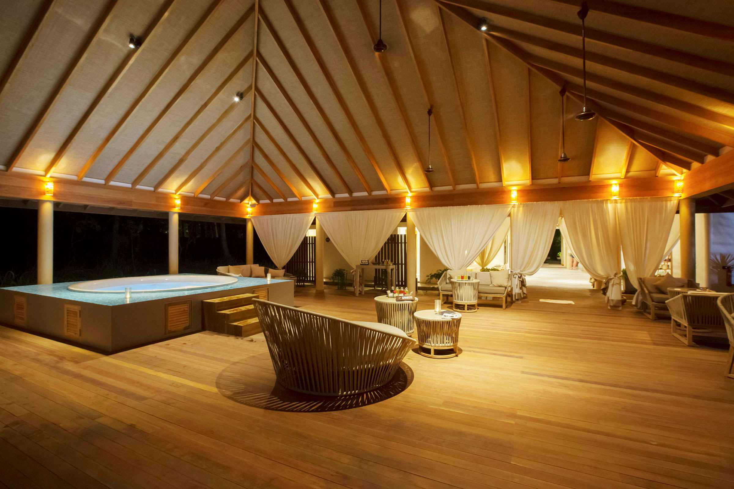 En luksuriøs udendørs lounge med pool og trämøbler, oplyst om aftenen. (AI-genereret tekst)