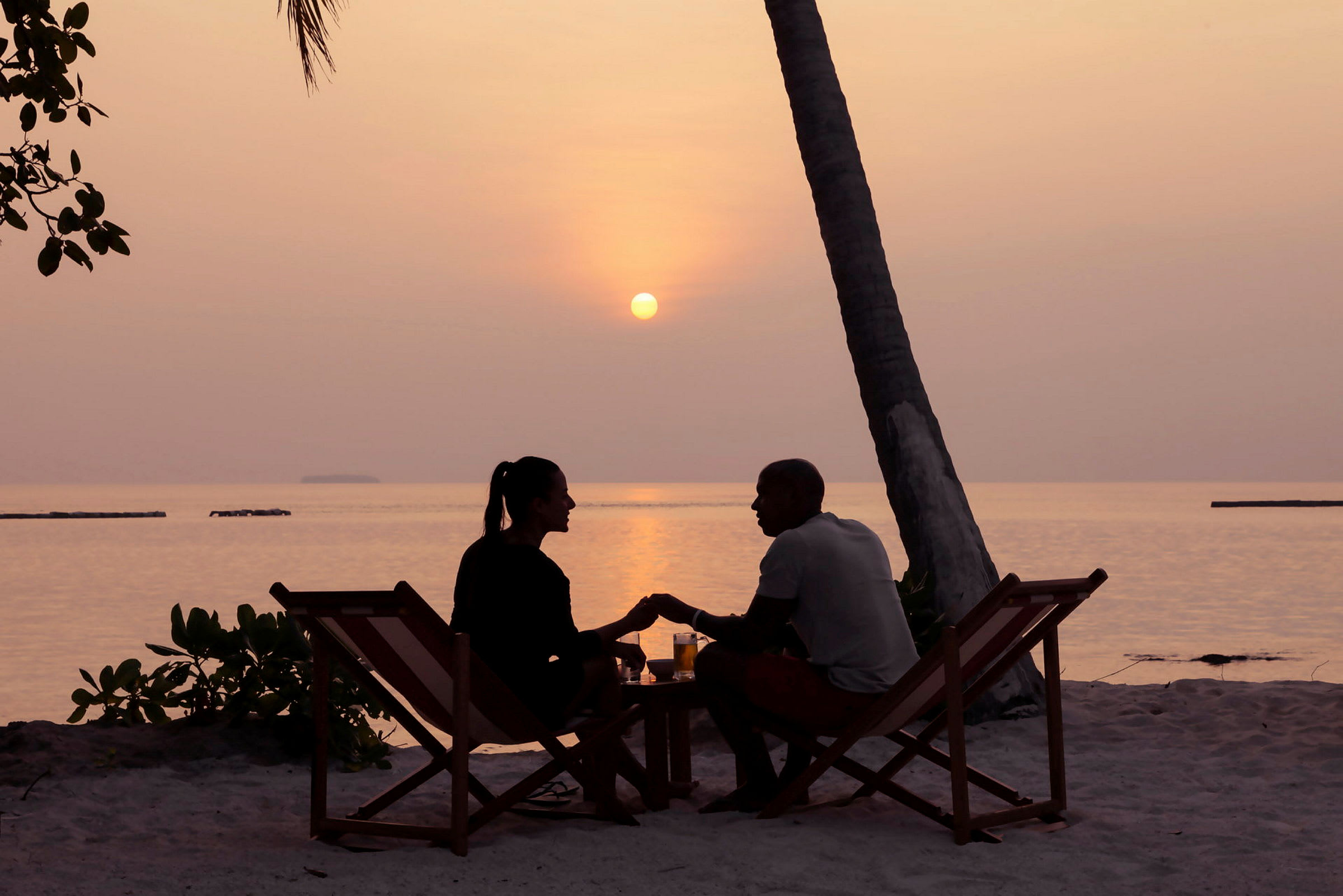 Et par sidder i liggestole på stranden under en solnedgang. (AI-genereret tekst)