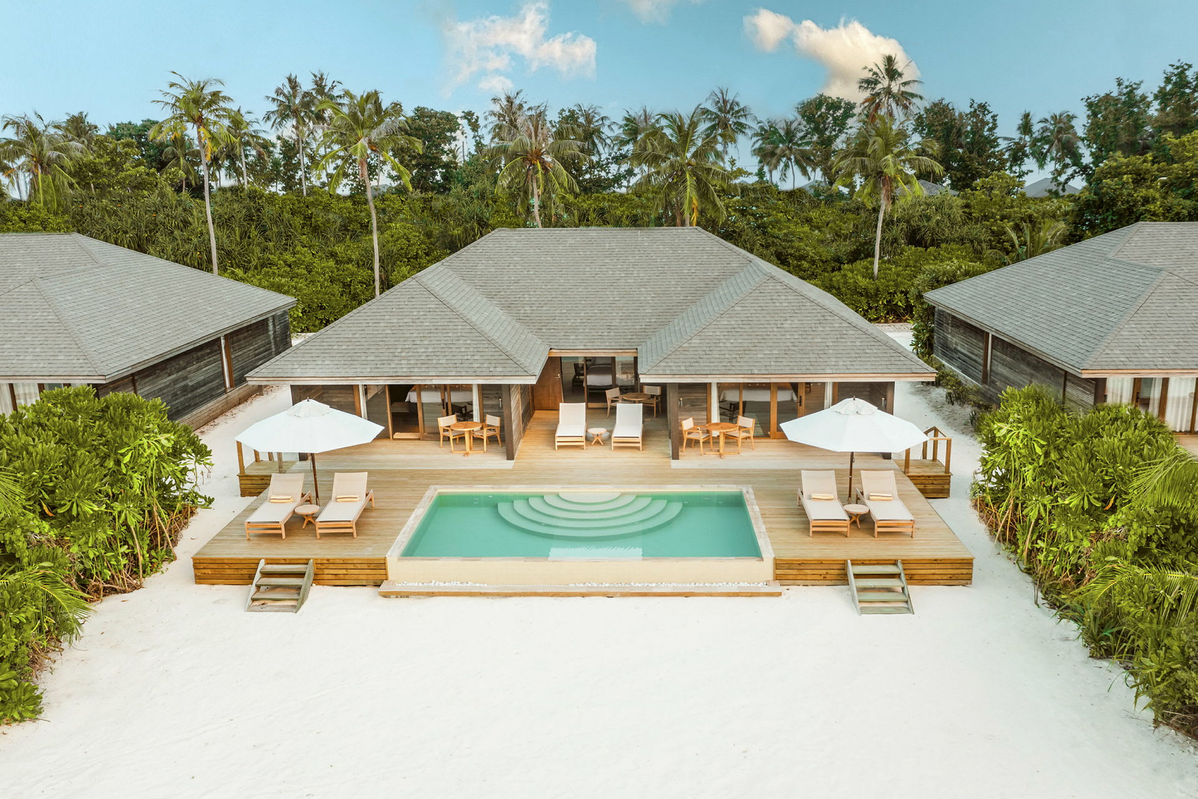 Villaer med private pools og solterrasser omgivet af grønt ved en hvid sandstrand. (AI-genereret tekst)