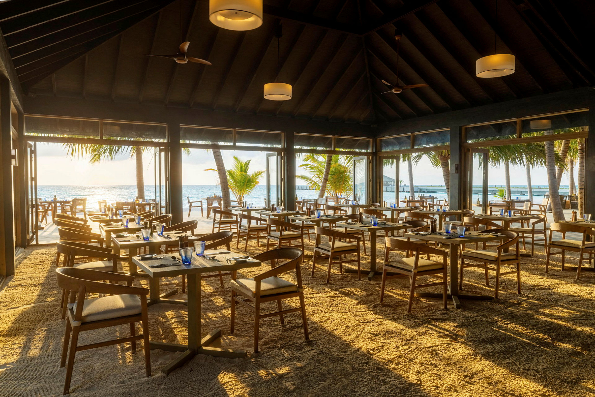 Restaurant med sandgulv og udsigt over havet og palmer. (AI-genereret tekst)