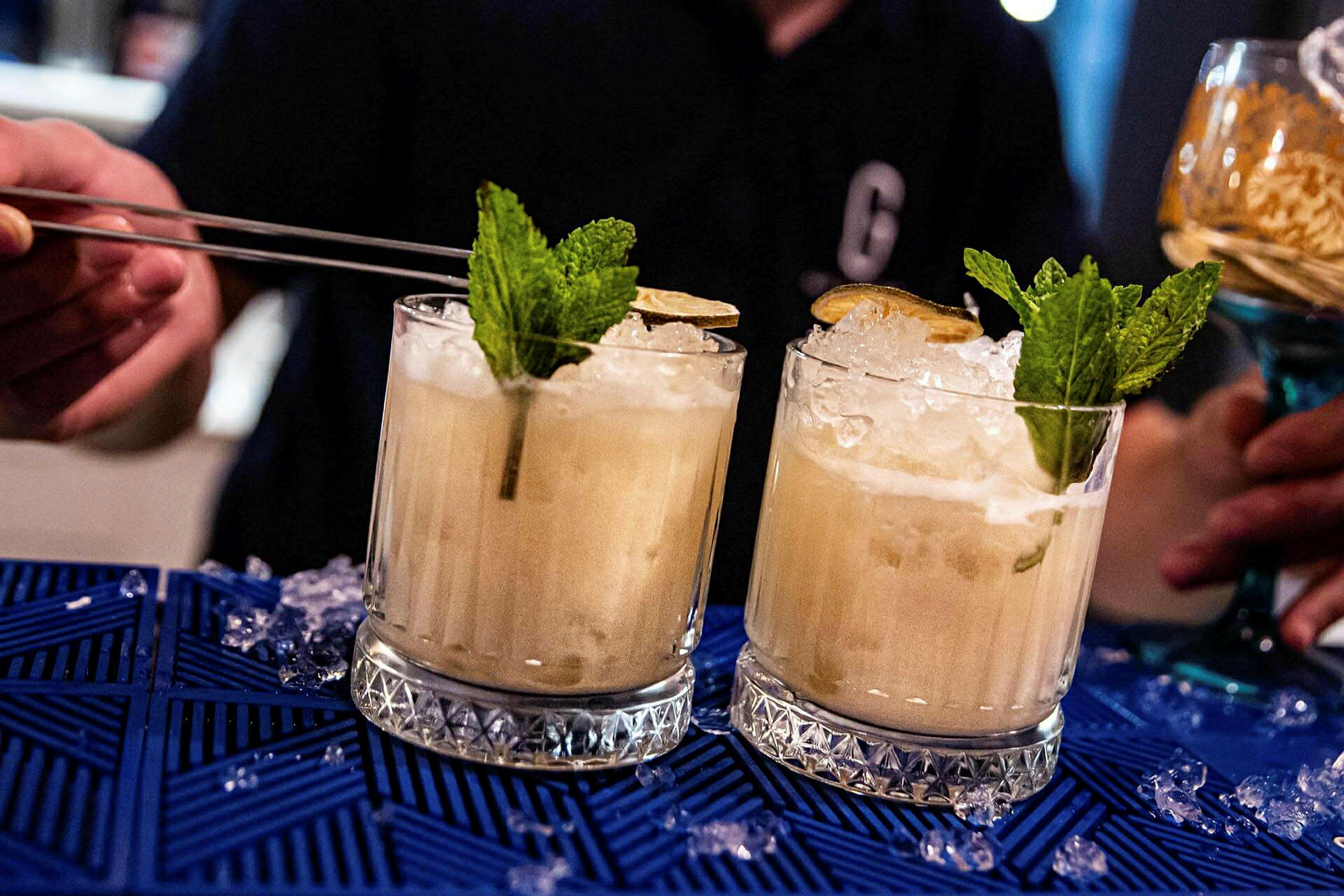 To cocktails med is, mynte og lime på blå dug. (AI-genereret tekst)
