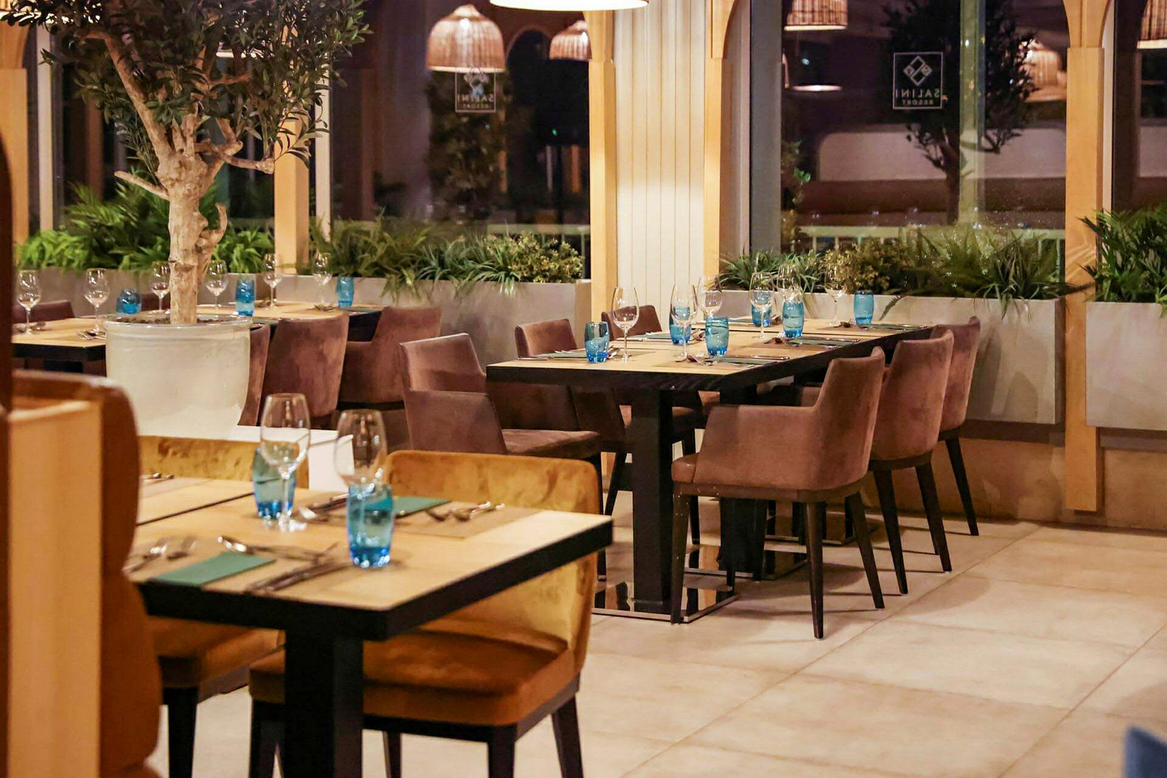 Et indbydende restaurantområde med dækkede borde og komfortable stole, omgivet af grønne planter. (AI-genereret tekst)