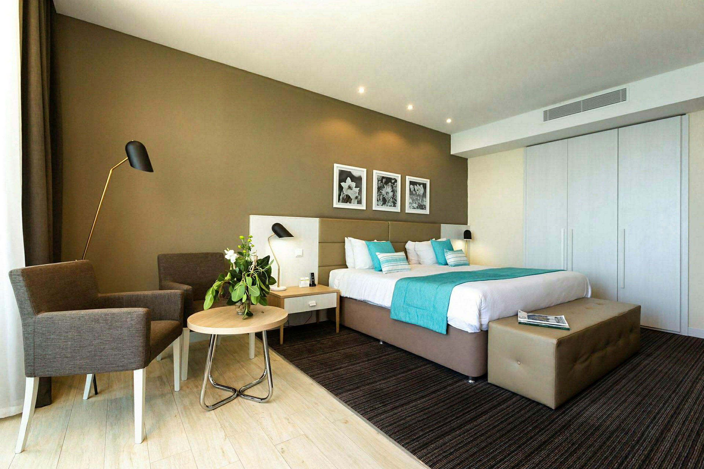 Et moderne indrettet hotelværelse med en stor seng, dekorative puder og et natbord. Et par lænestole står ved siden af et lille bord. (AI-genereret tekst)