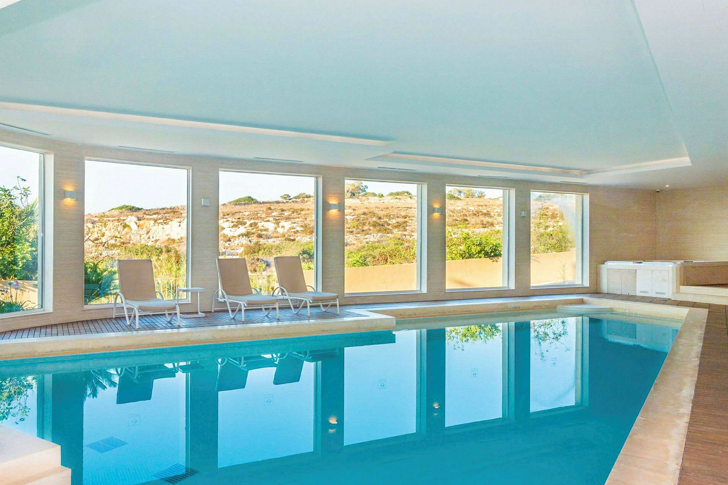 Indendørs pool med store vinduer og nogle liggestole ved siden af. (AI-genereret tekst)
