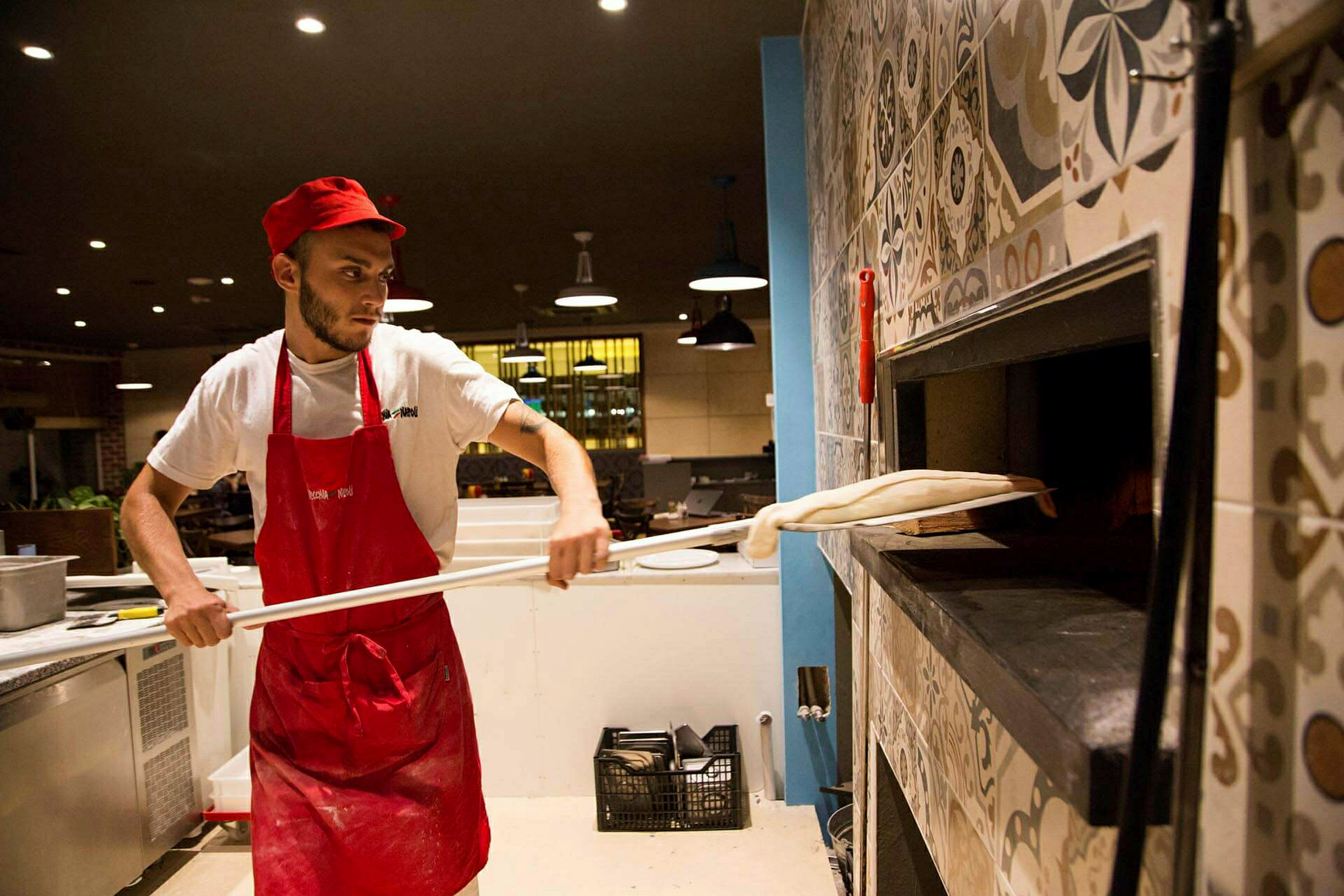 En kok i arbejdstøj forbereder en pizza og placerer den i en brændefyret ovn. (AI-genereret tekst)