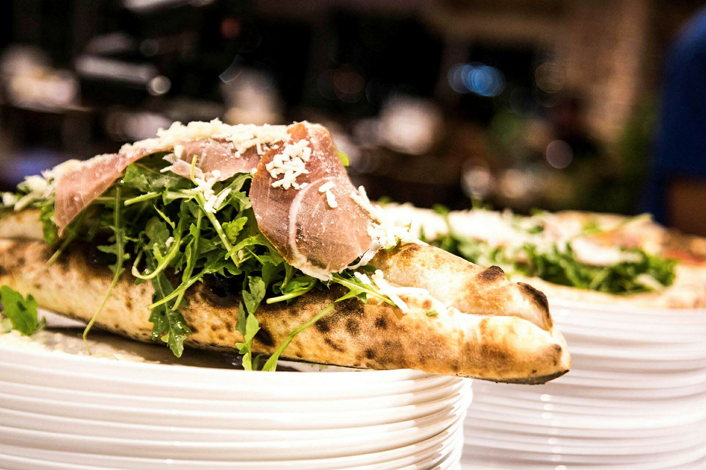 Et nærbillede af en pizza med rucolasalat og skinke, toppet med revet ost, serveret på en tallerken. (AI-genereret tekst)