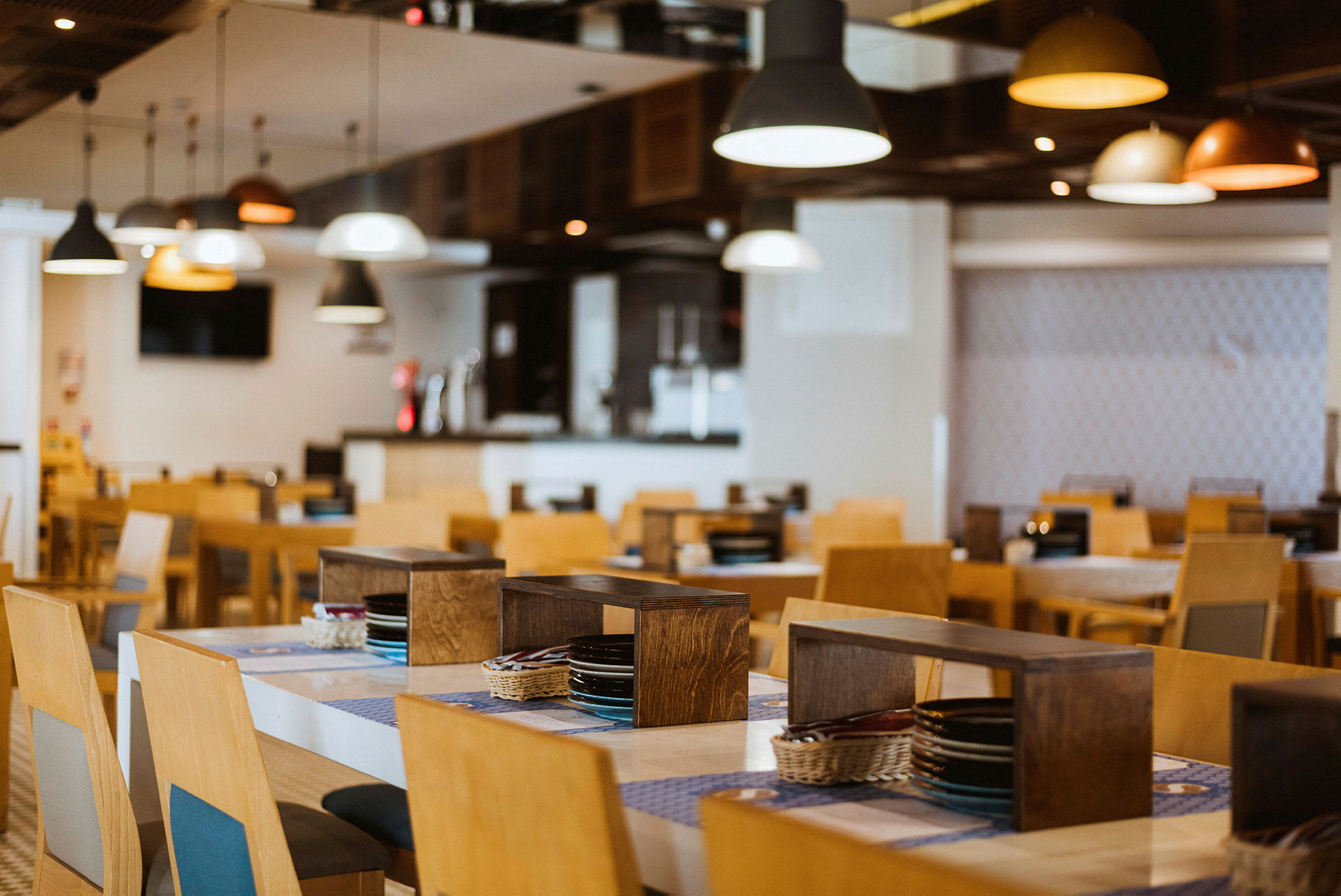 Restaurant med træborde og stole, oplyst af loftlamper. (AI-genereret tekst)