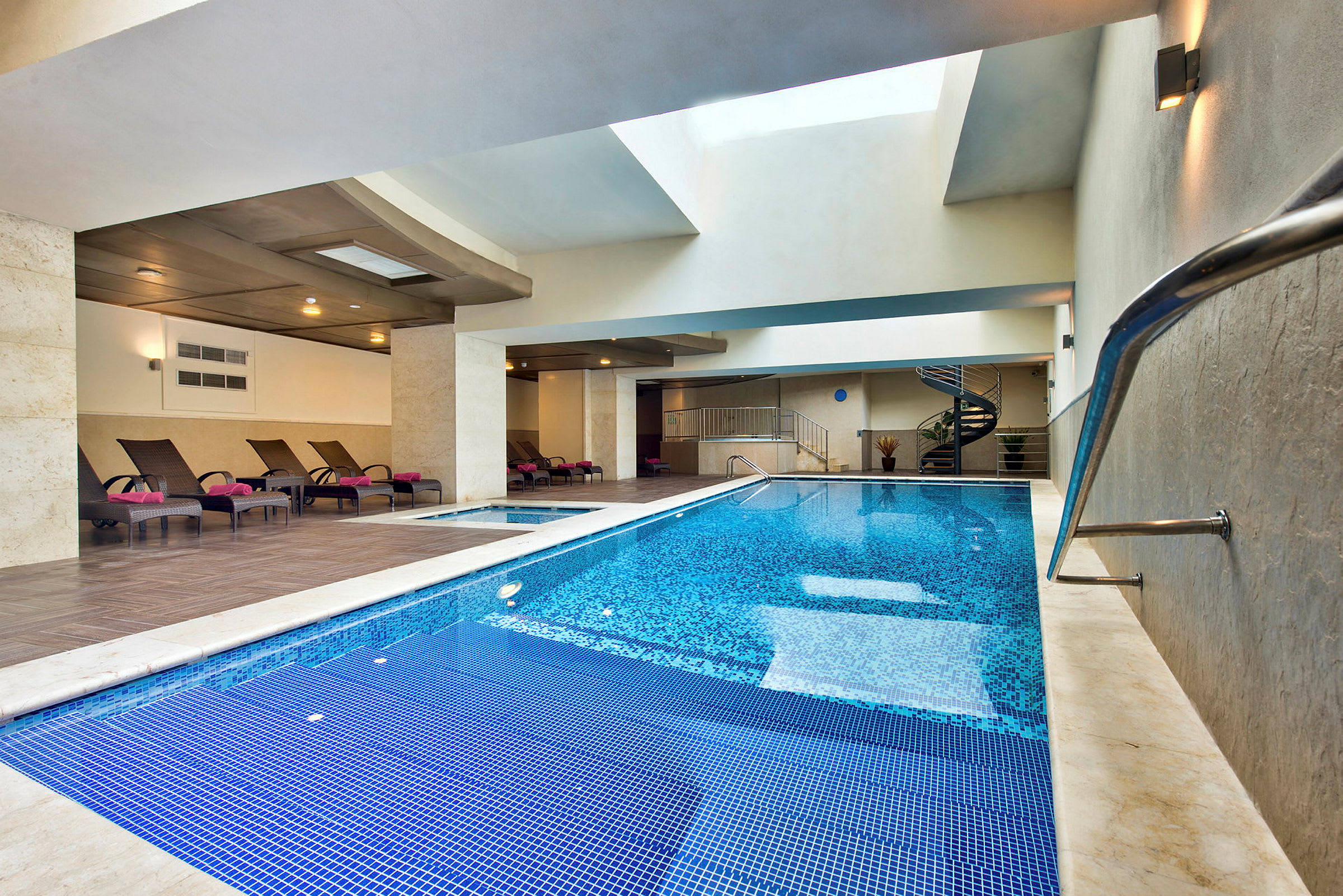 Indendørs pool med liggestole og moderne design. (AI-genereret tekst)