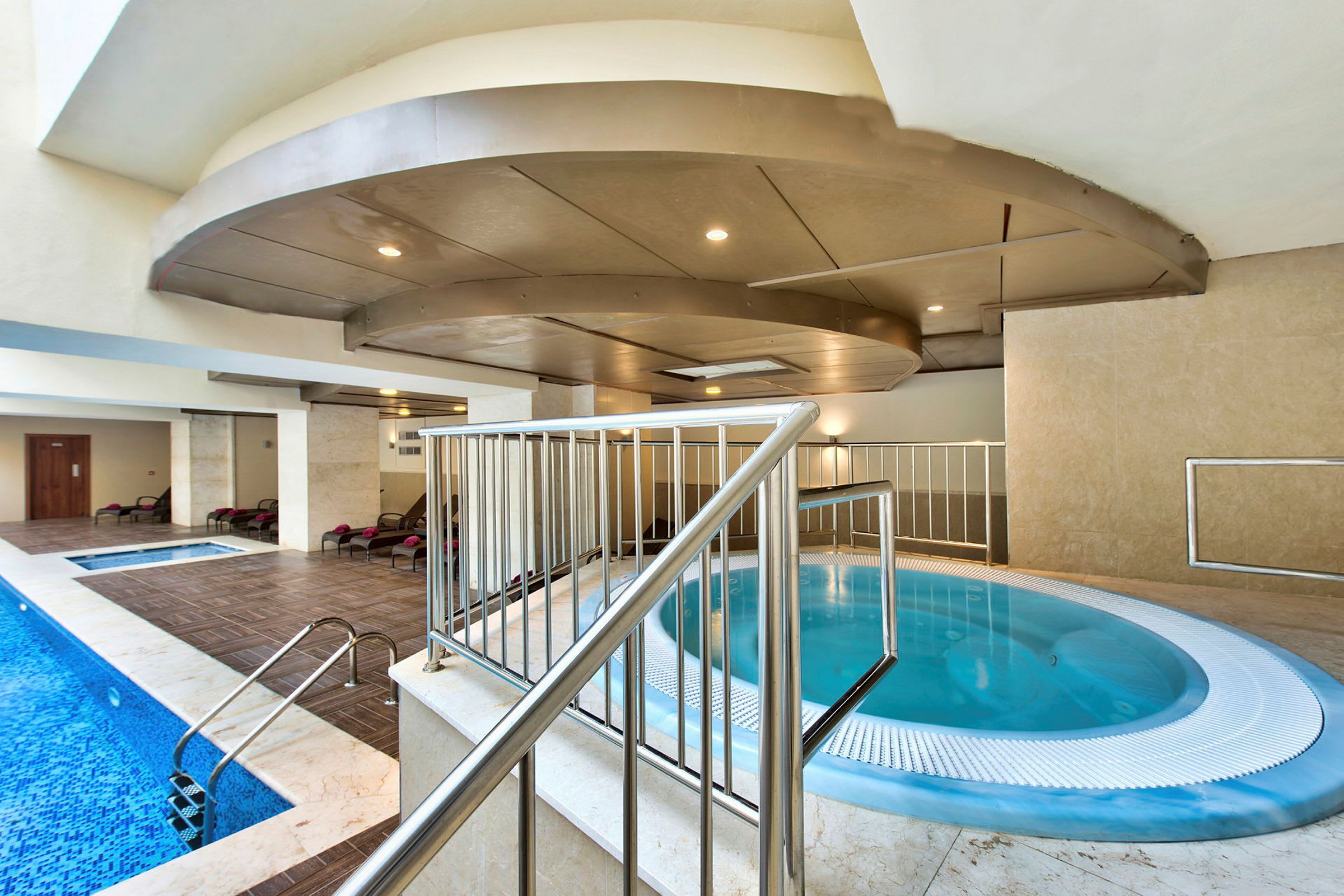 En indendørs pool med jacuzzi og liggestole. (AI-genereret tekst)