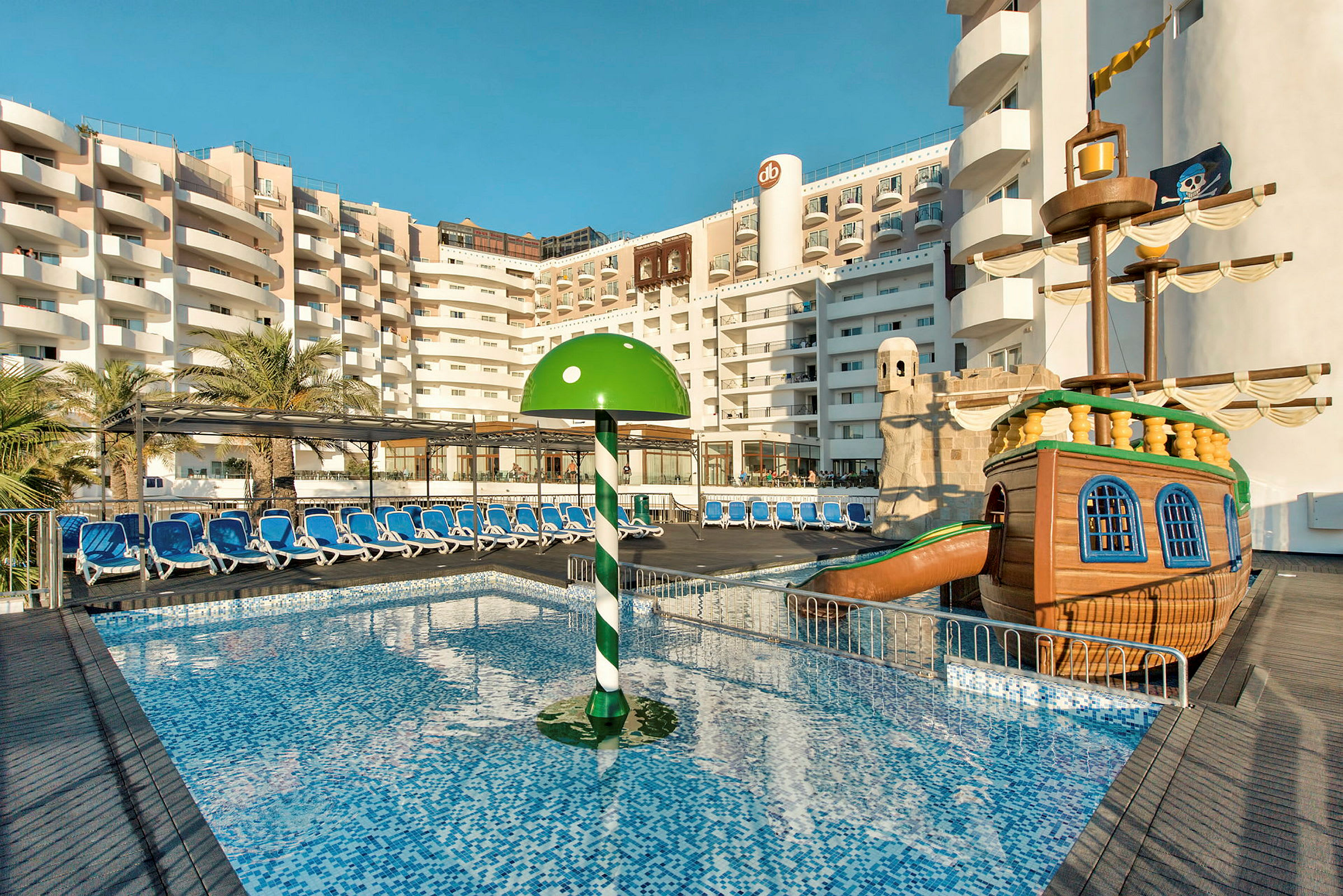 En hotelpool med liggestole, en grøn parasol og en legetøjspiratskib. (AI-genereret tekst)