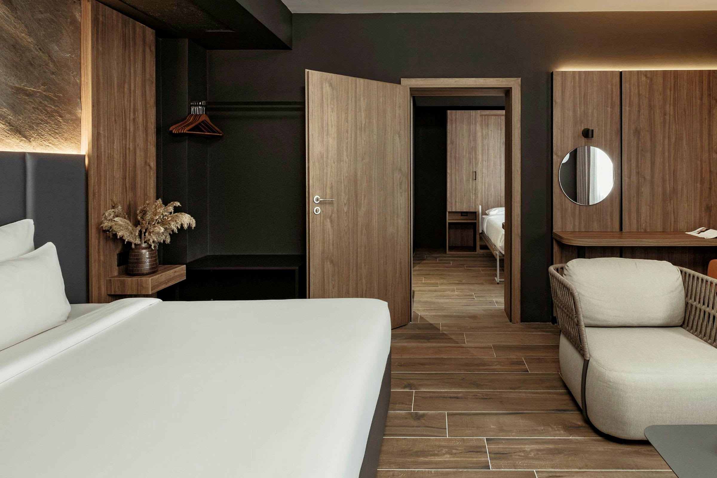 Et moderne hotelværelse med mørke træmøbler og minimalistisk design. En seng, en lænestol og et skrivebord er synlige i rummet. (AI-genereret tekst)
