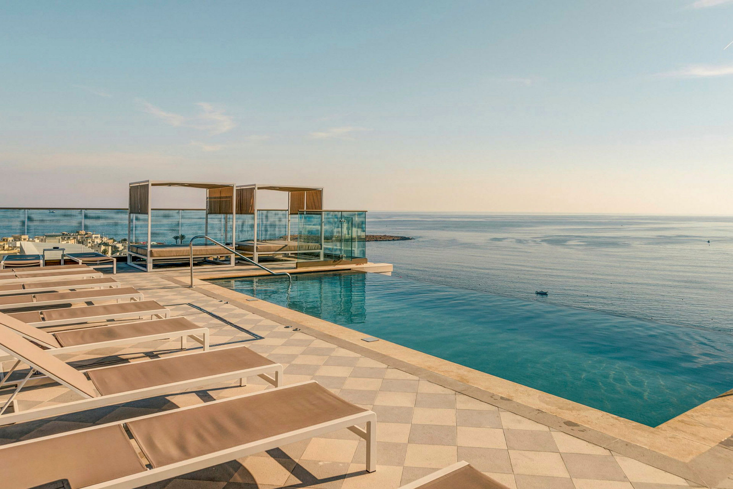 En infinitypool ved havet med liggestole og skyggefulde cabanas samt et rækværk mod vandet. (AI-genereret tekst)