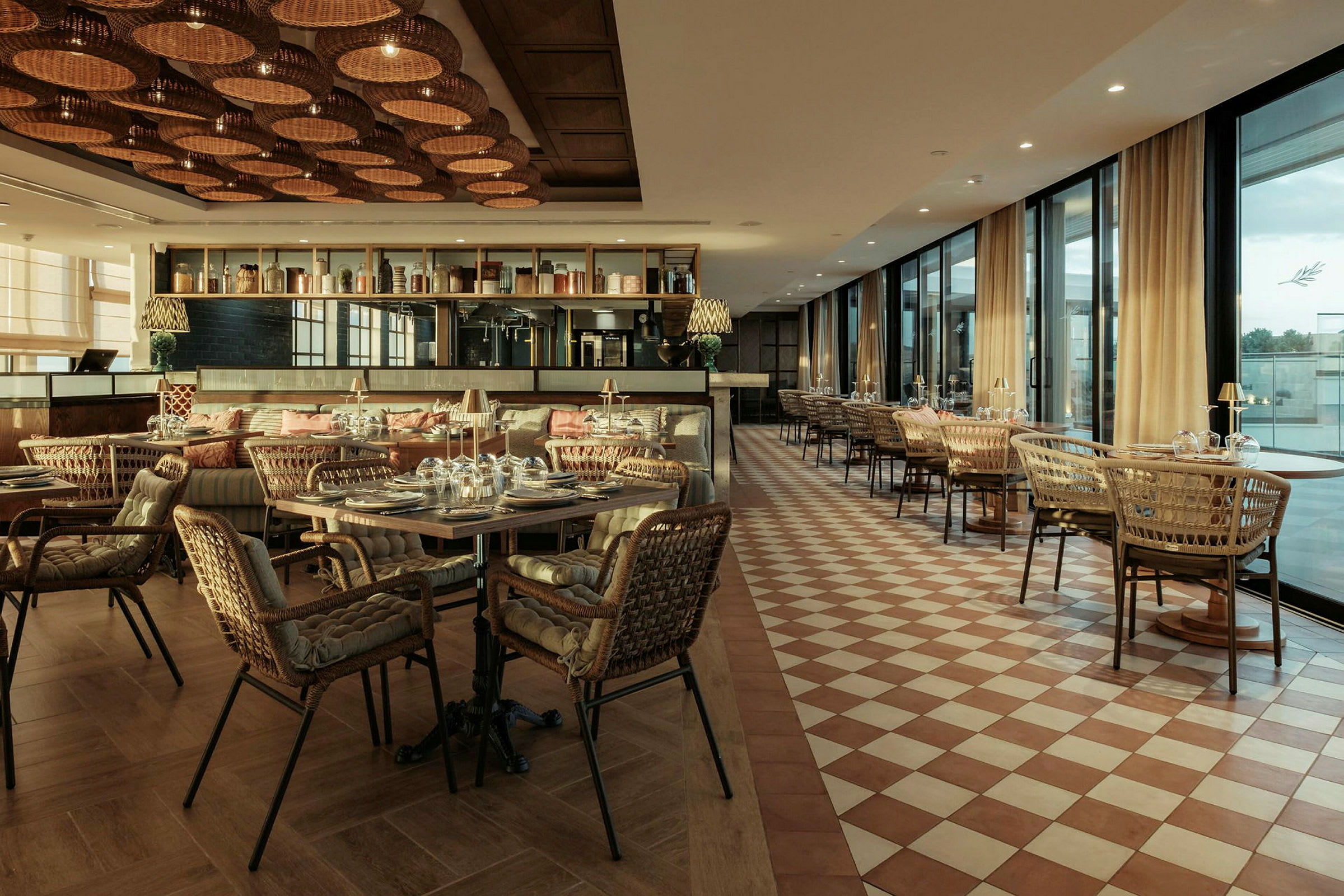 En smagfuldt indrettet restaurant med borde og kurvestole. Gulvet har et ternmønster, og loftet er dekoreret med flettede lamper. (AI-genereret tekst)