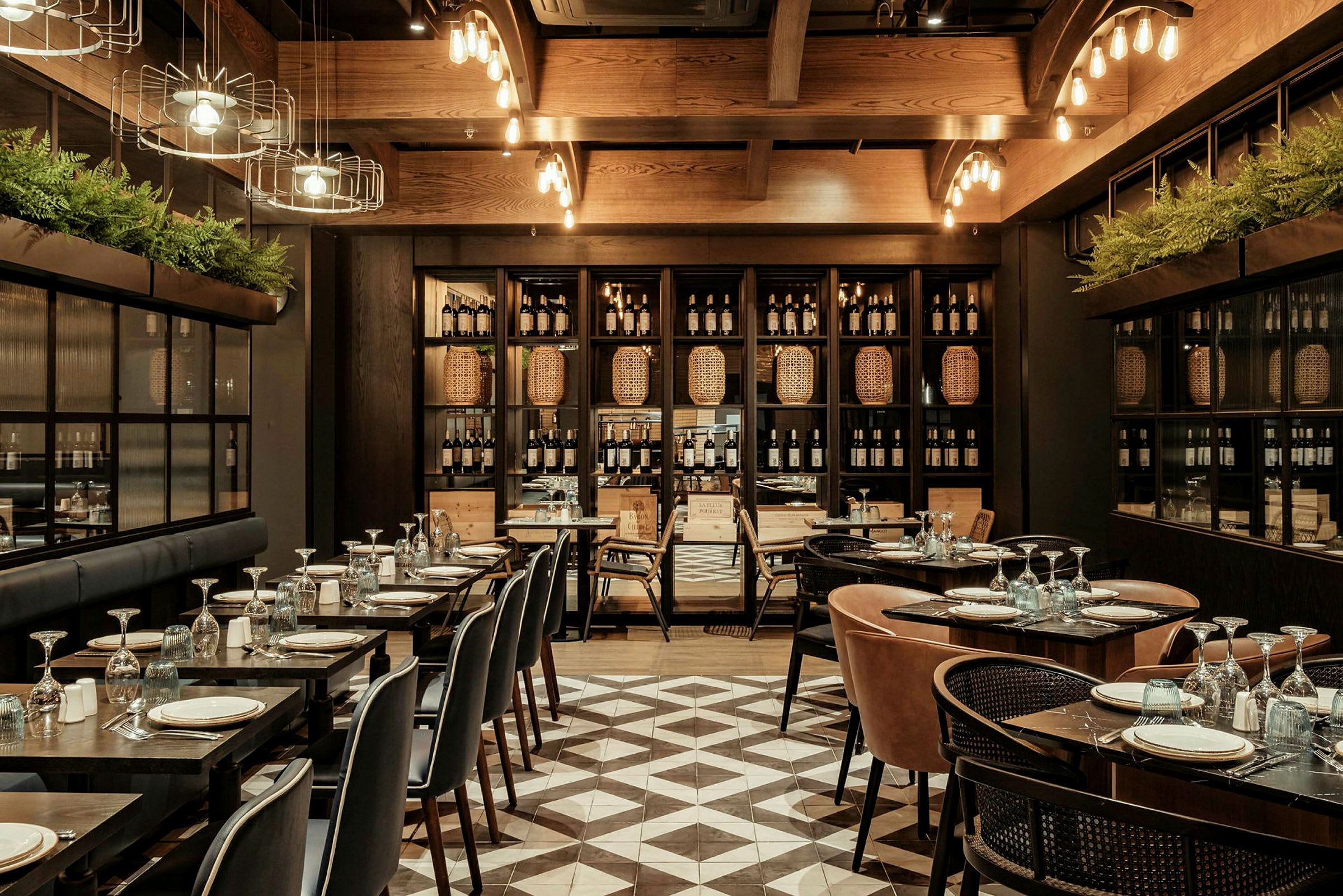 Et elegant restaurantområde med dækkede borde, komfortable stole og en reolvæg fyldt med vinflasker og kurve. (AI-genereret tekst)