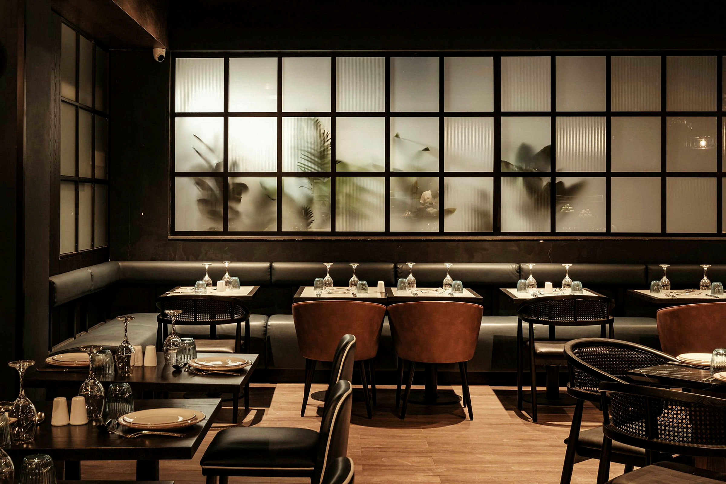 En elegant restaurant med mørkt interiør, dækkede borde og stole foran matterede glasvinduer. (AI-genereret tekst)
