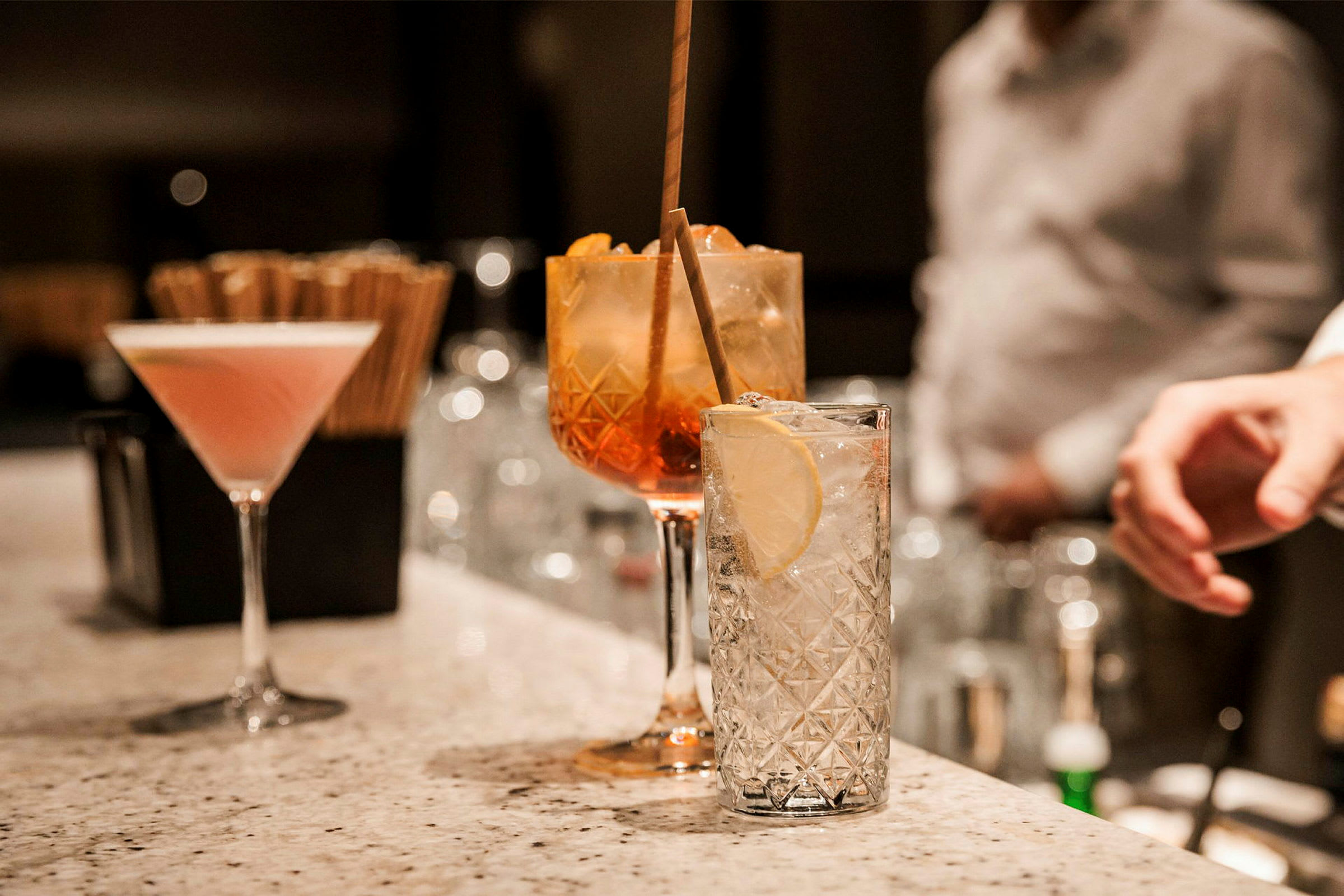 Flere glas med forskellige cocktails står på en bardisk i marmor. (AI-genereret tekst)