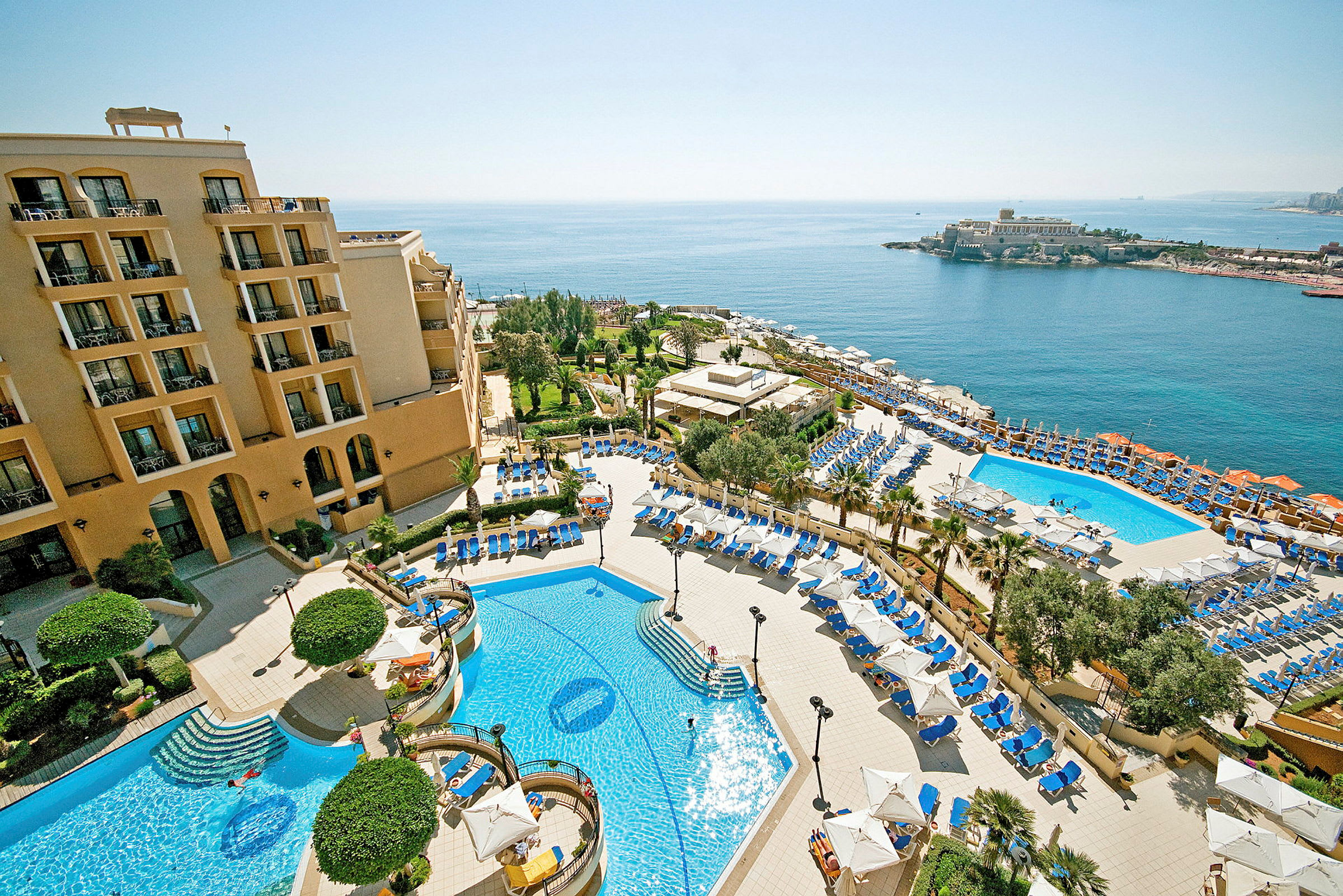 Et hotelanlæg med pools, liggestole og parasoller samt havudsigt. (AI-genereret tekst)