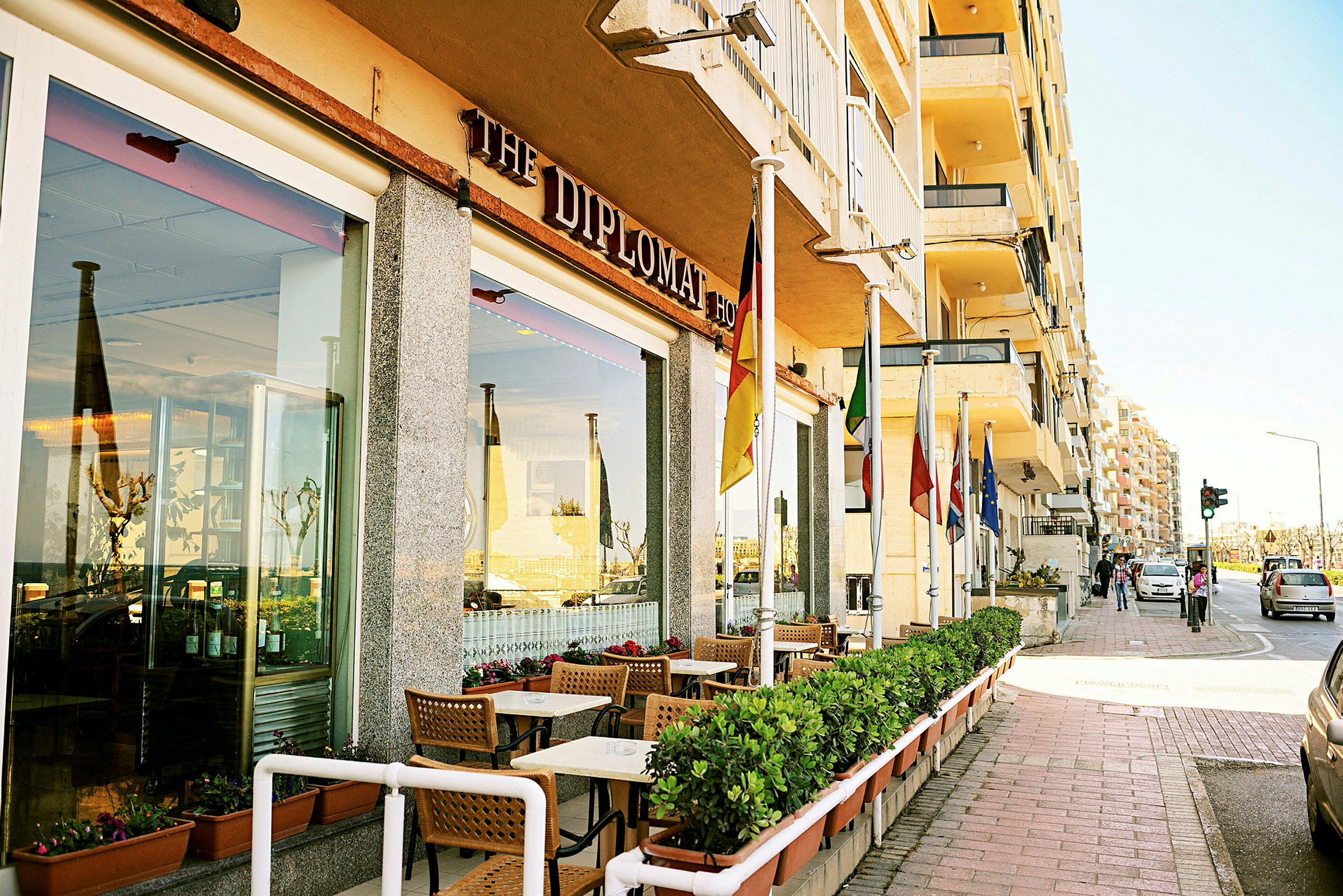 Restaurant med udendørs servering og forskellige flag ved indgangen langs en fortov. (AI-genereret tekst)