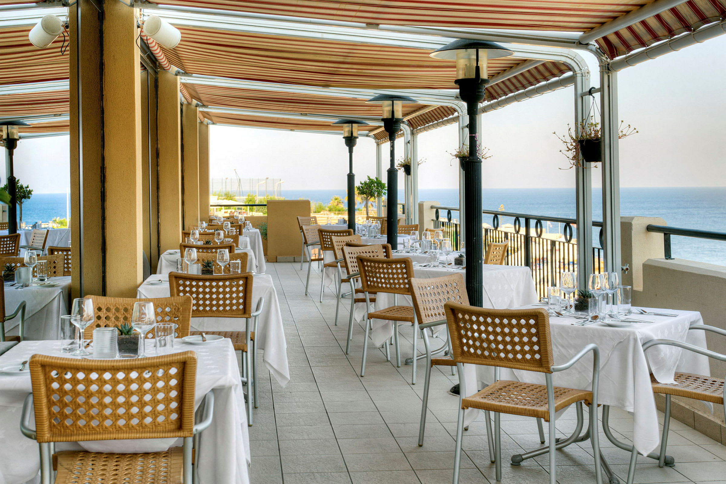 En restaurantterrasse med dækkede borde og udsigt over havet. (AI-genereret tekst)