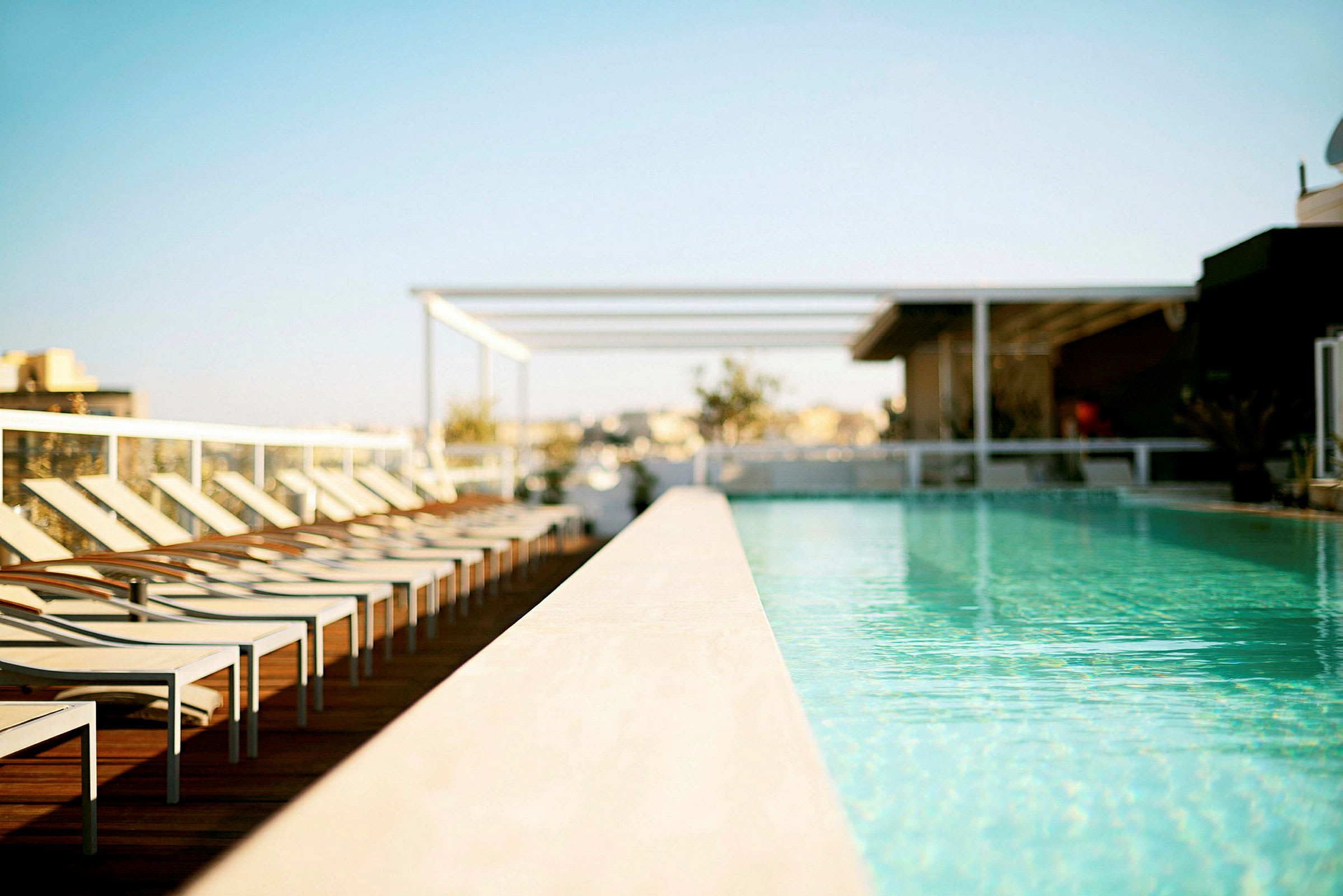 Billede af en udendørs swimmingpool omgivet af liggestole og en klar blå himmel i baggrunden. (AI-genereret tekst)