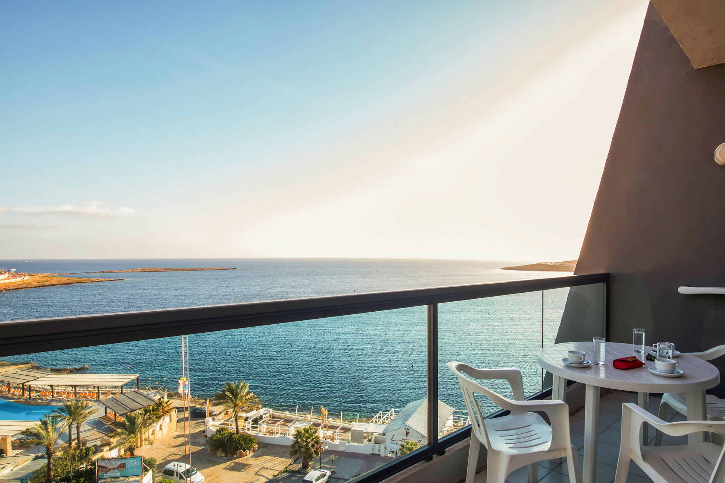 En balkon med et bord og stole, med udsigt over havet og det omkringliggende landskab. (AI-genereret tekst)