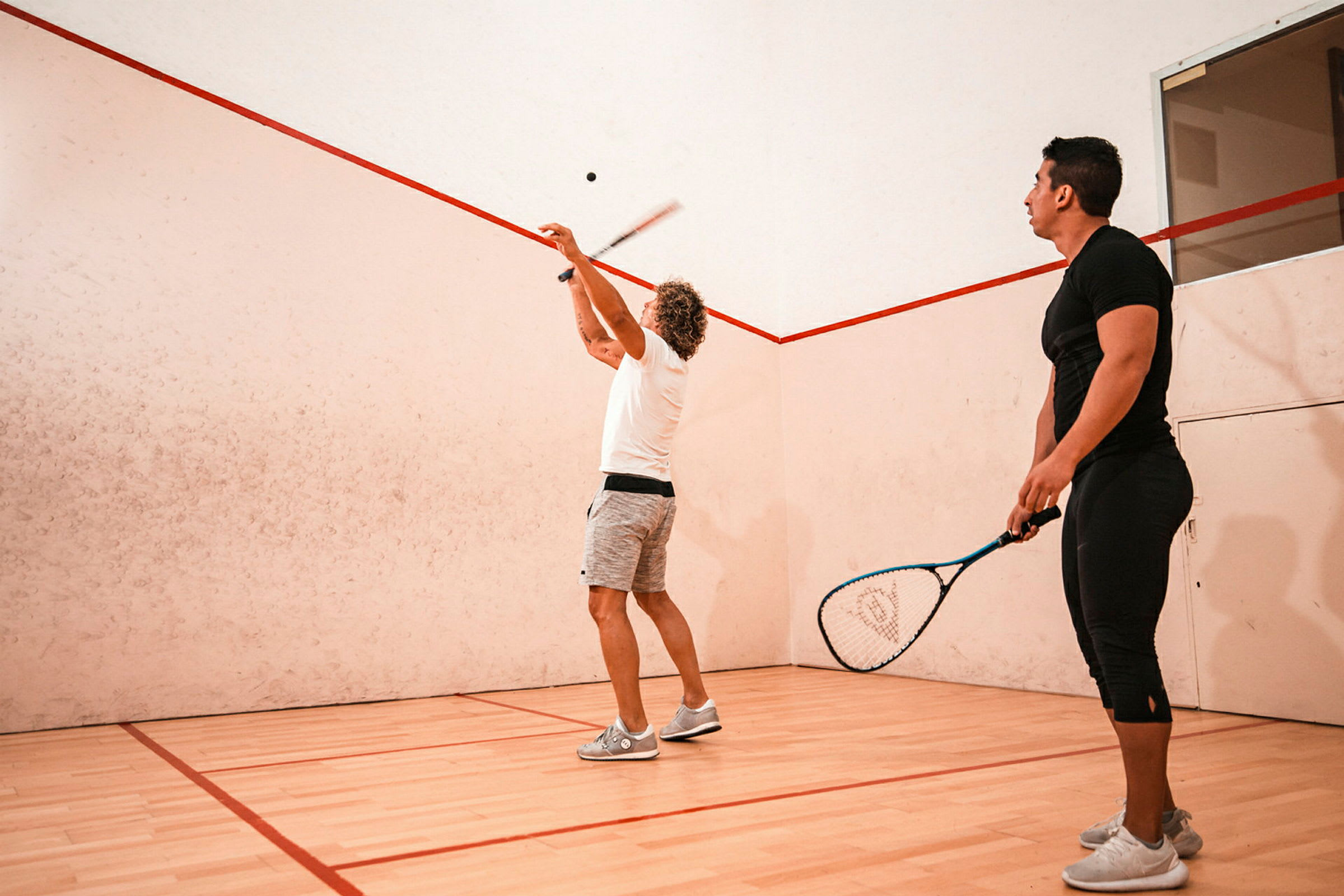 Personer spiller squash på en indendørsbane. (AI-genereret tekst)